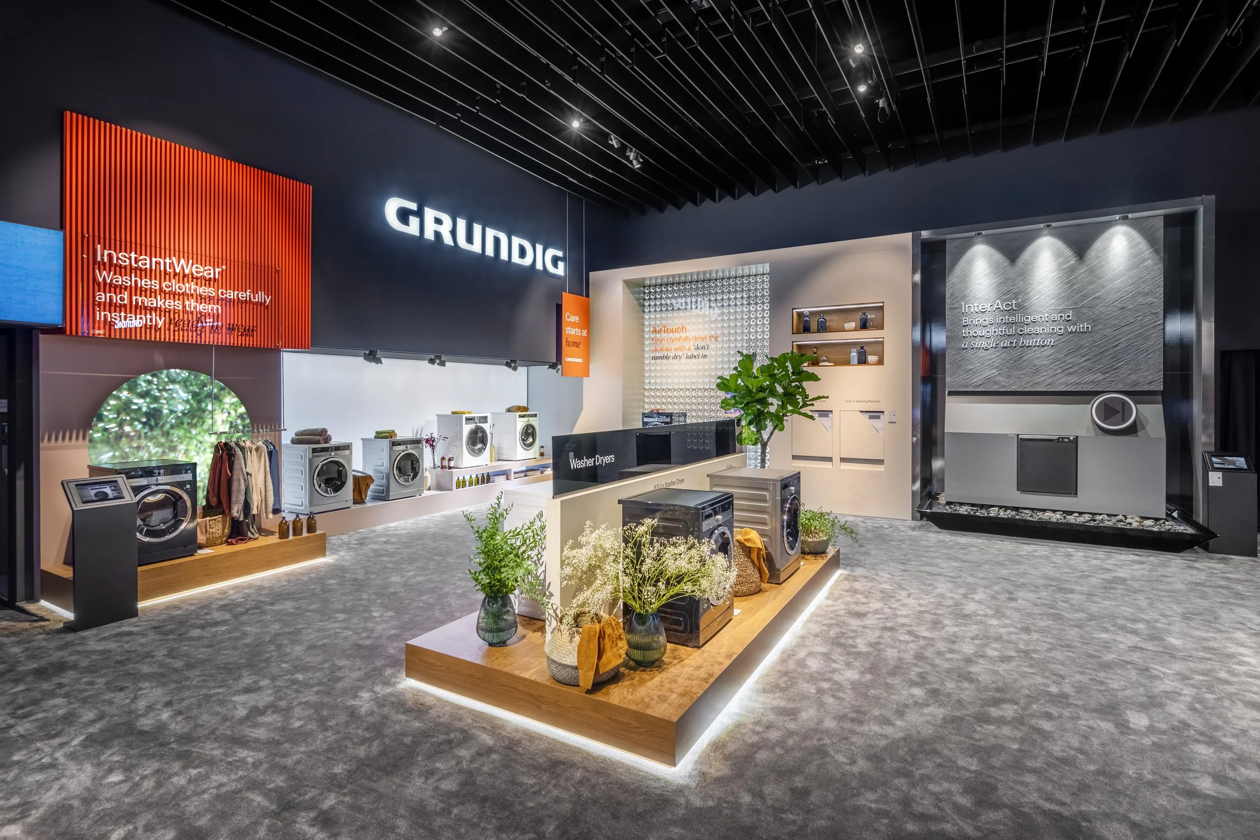 Interior of a showroom featuring Grundig appliances, including washing machines, dryer displays, and informational displays with plants and lighting.