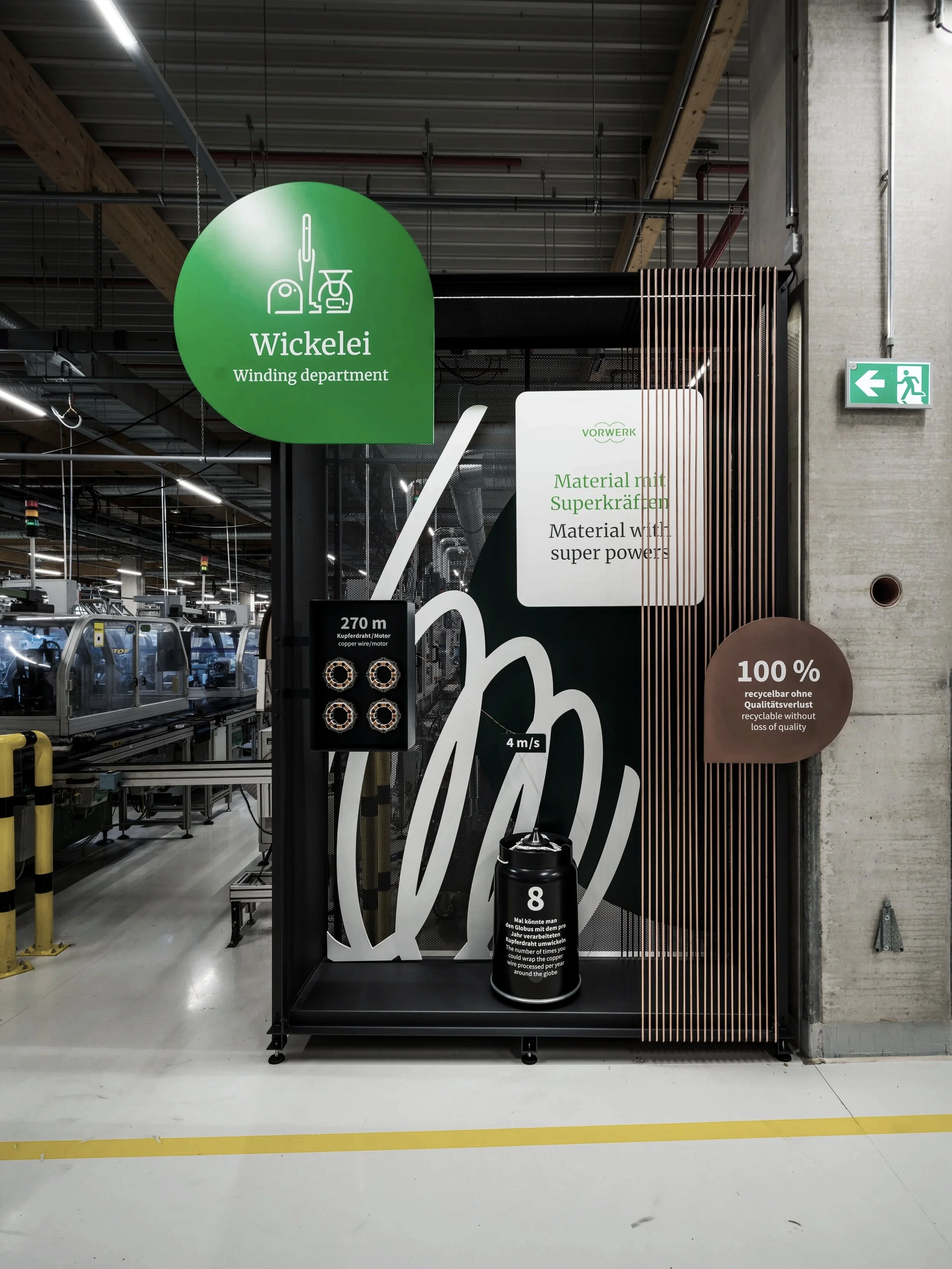 Sign in a factory highlighting the Wickelei winding department, with information about superpower materials and qualities, a graphic of a hand with a tension of 4 m/s, copper wire, and an 8-liter container.
