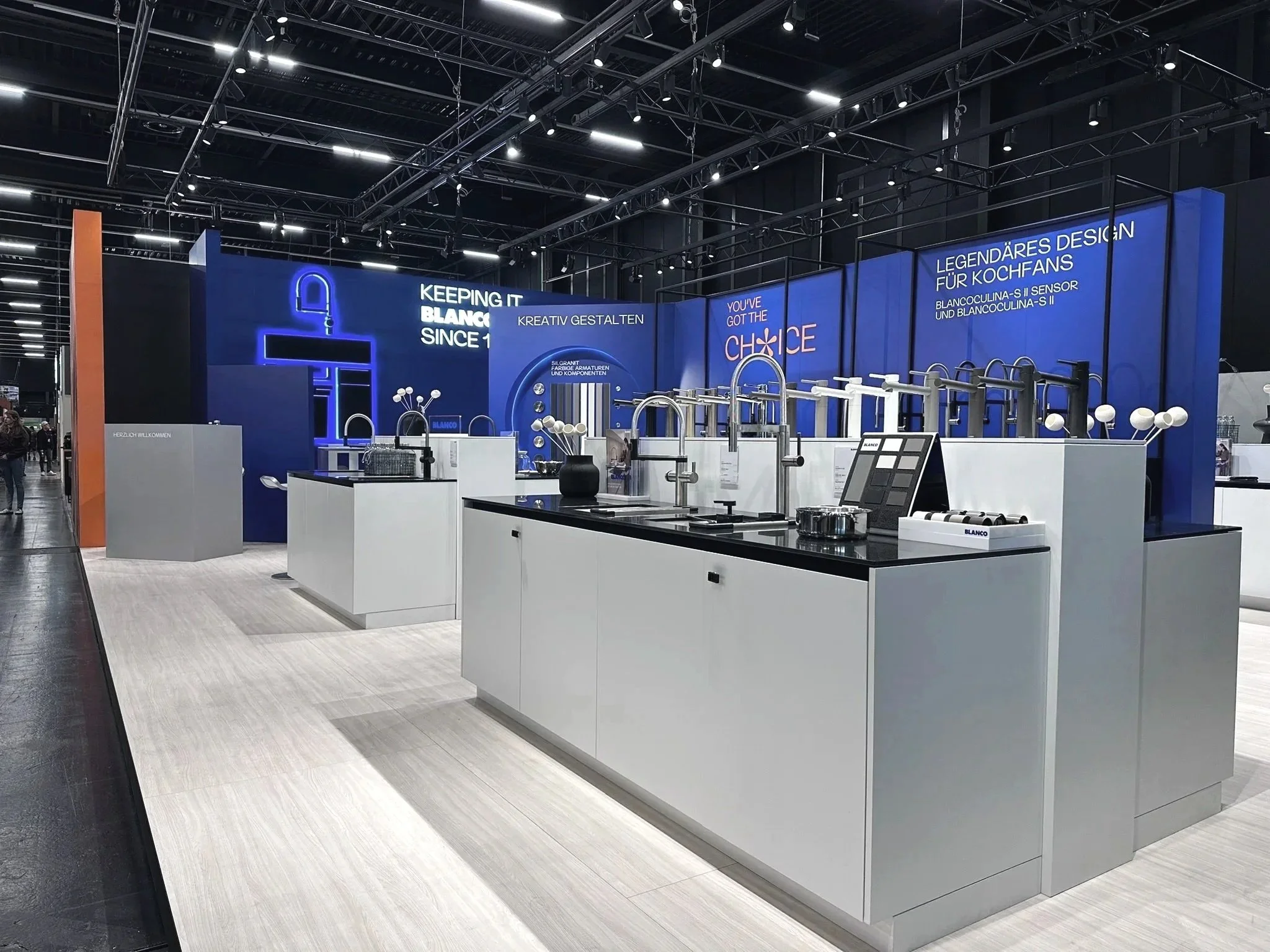 Trade show booth featuring modern kitchen faucets and fixtures, with a blue-themed backdrop displaying the brand name Blanco and related slogans.