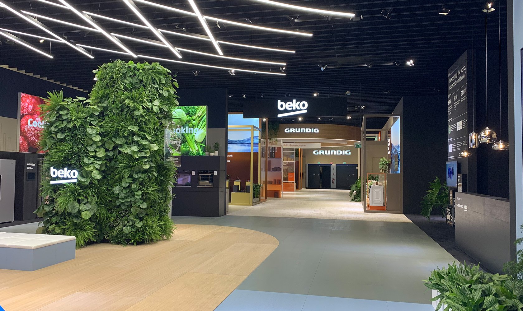 Interior view of an appliance store with the brands Beko and Grundig, green plants, digital screens, and modern lighting.