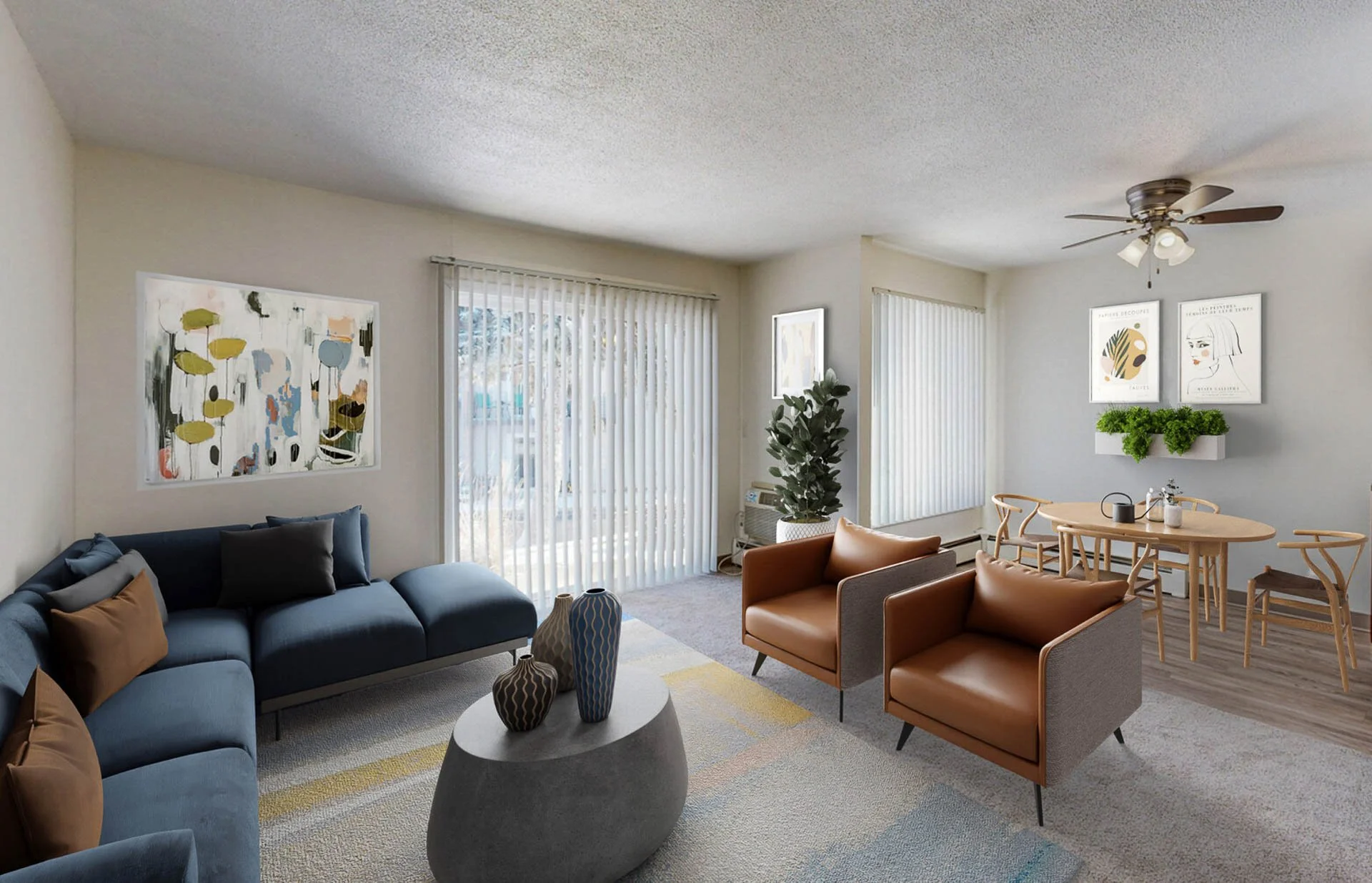 Living room with a dark blue sofa, brown armchairs, a round coffee table with decorative vases, and a dining area with a light wood table and chairs. Large windows with vertical blinds, abstract wall art, and a ceiling fan.