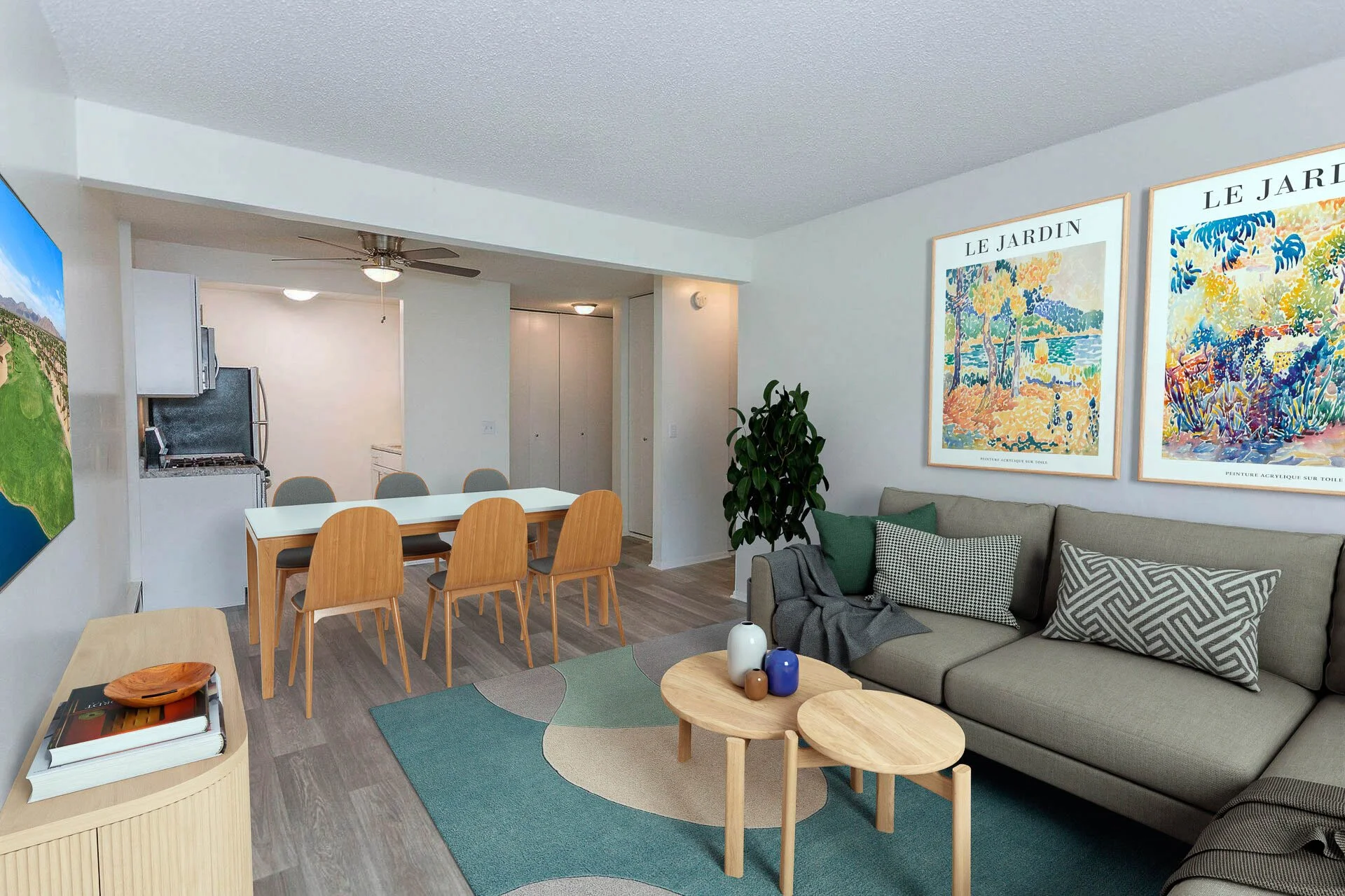 Living room with a gray sofa, patterned pillows, wooden coffee tables, colorful vases, abstract wall art, a dining area with chairs, a kitchen in the background, and a ceiling fan.