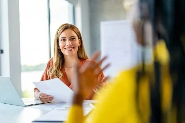 Woman smiling during a conversation in a bright office with large windows.