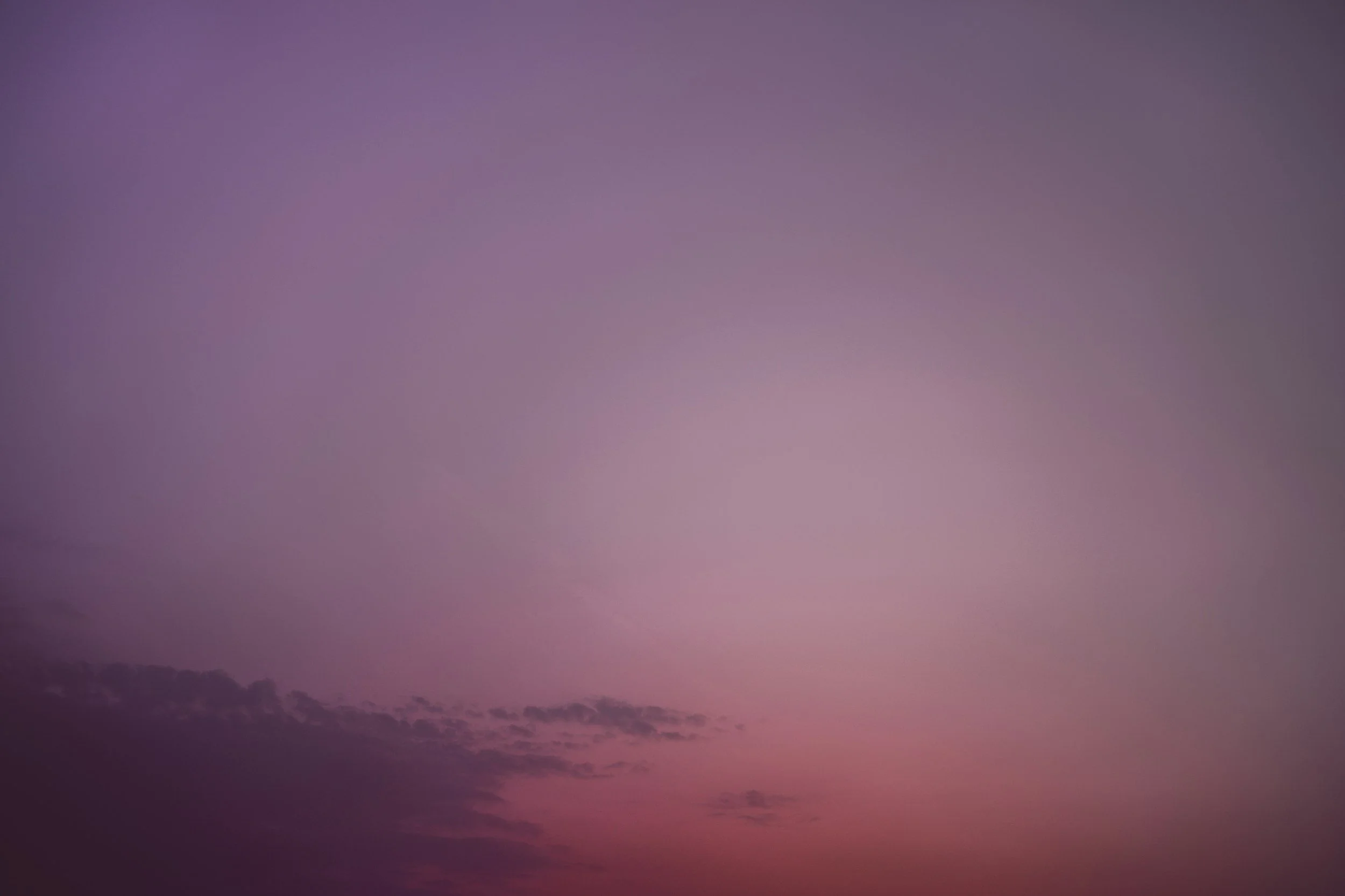 A clear sky at dusk with pink and purple hues and some thin clouds near the horizon.