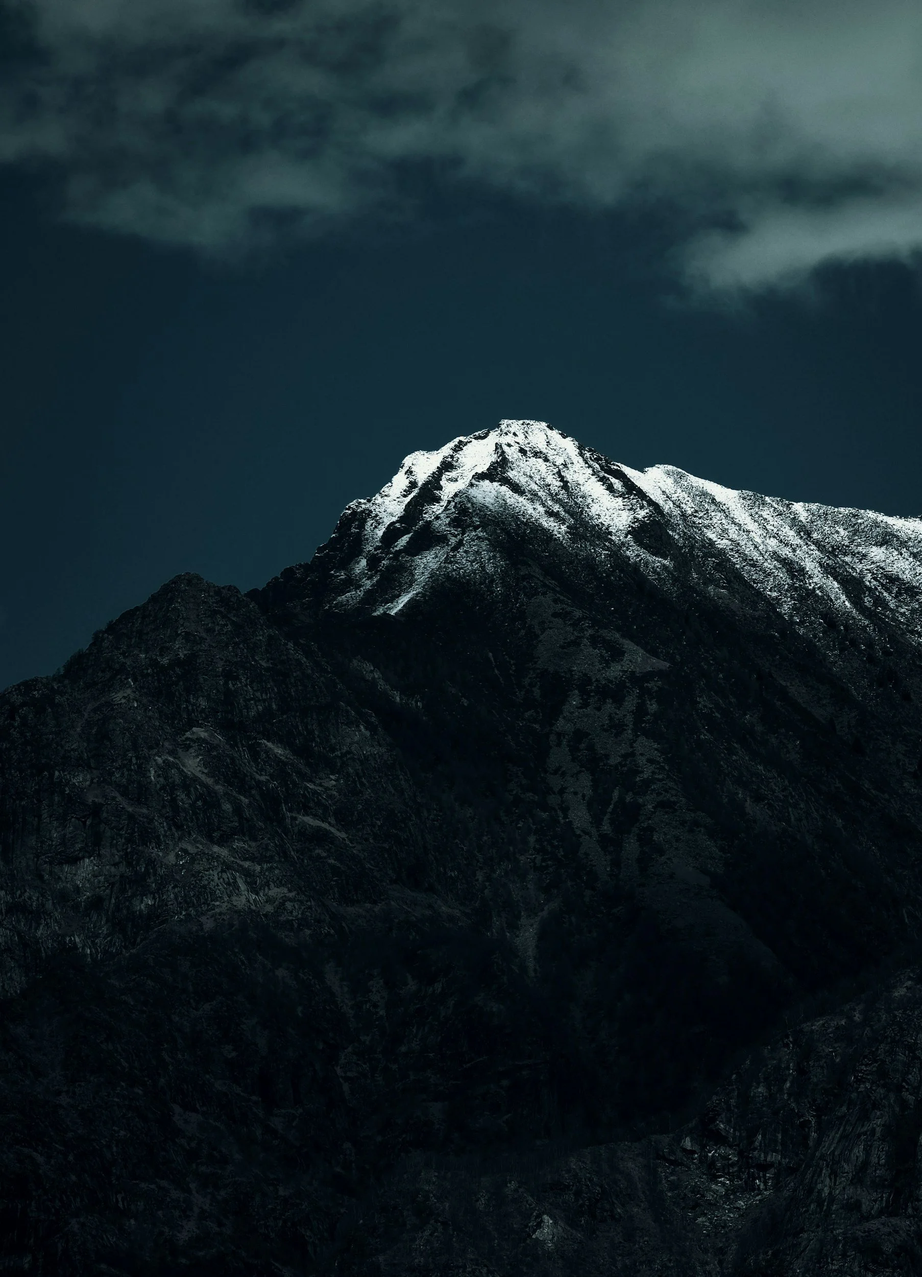 Snow-capped mountain peak under a cloudy night sky.