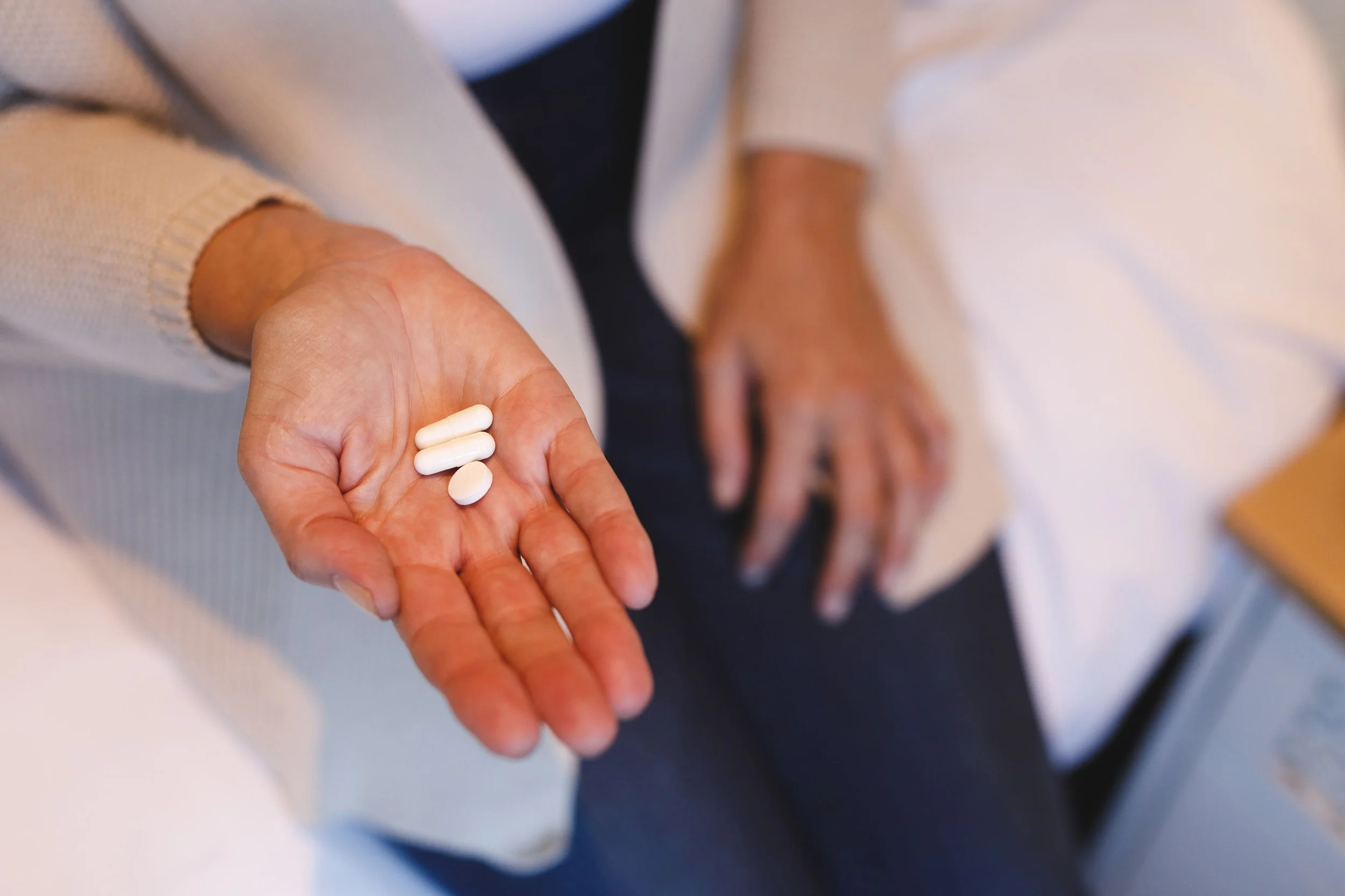 Close-up of a person's hand holding several white pills or tablets with a person in a white shirt in the background.