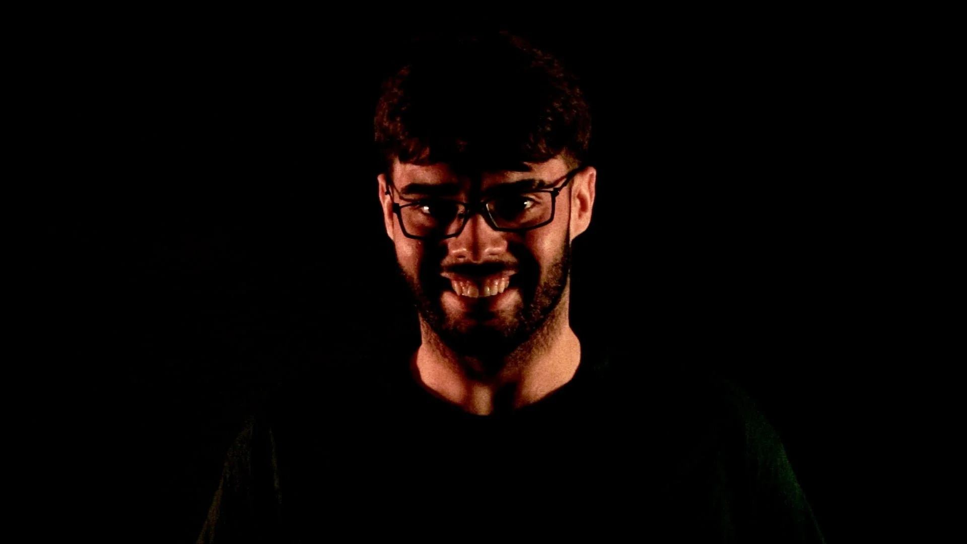A man with glasses smiling against a black background.
