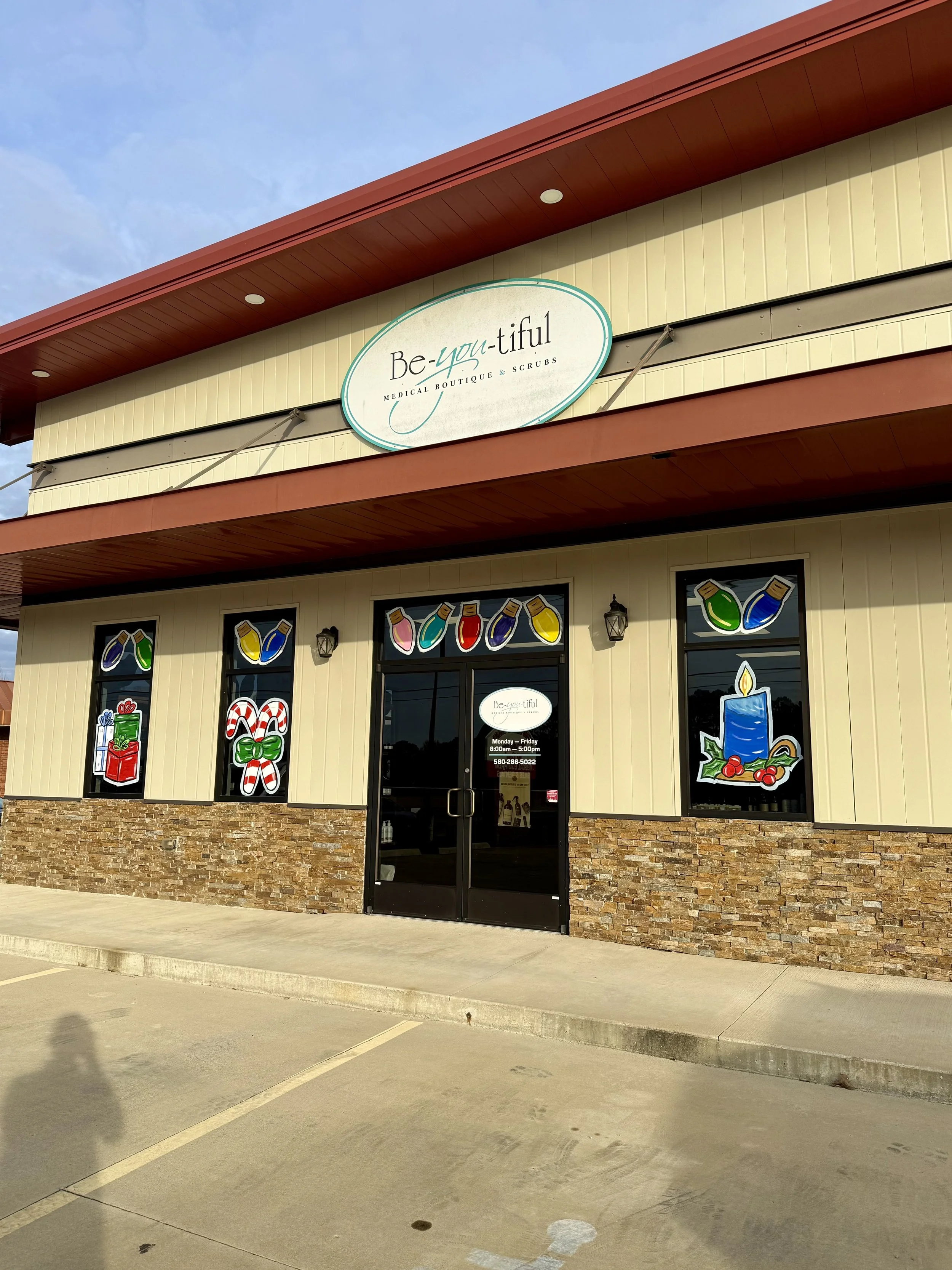 Outside view of a beauty and skincare store named Be-y- tiful Medical Boutique & Scrubs, with festive holiday window decorations including candles, gift boxes, candy canes, and painted bottles of lotion or serum.