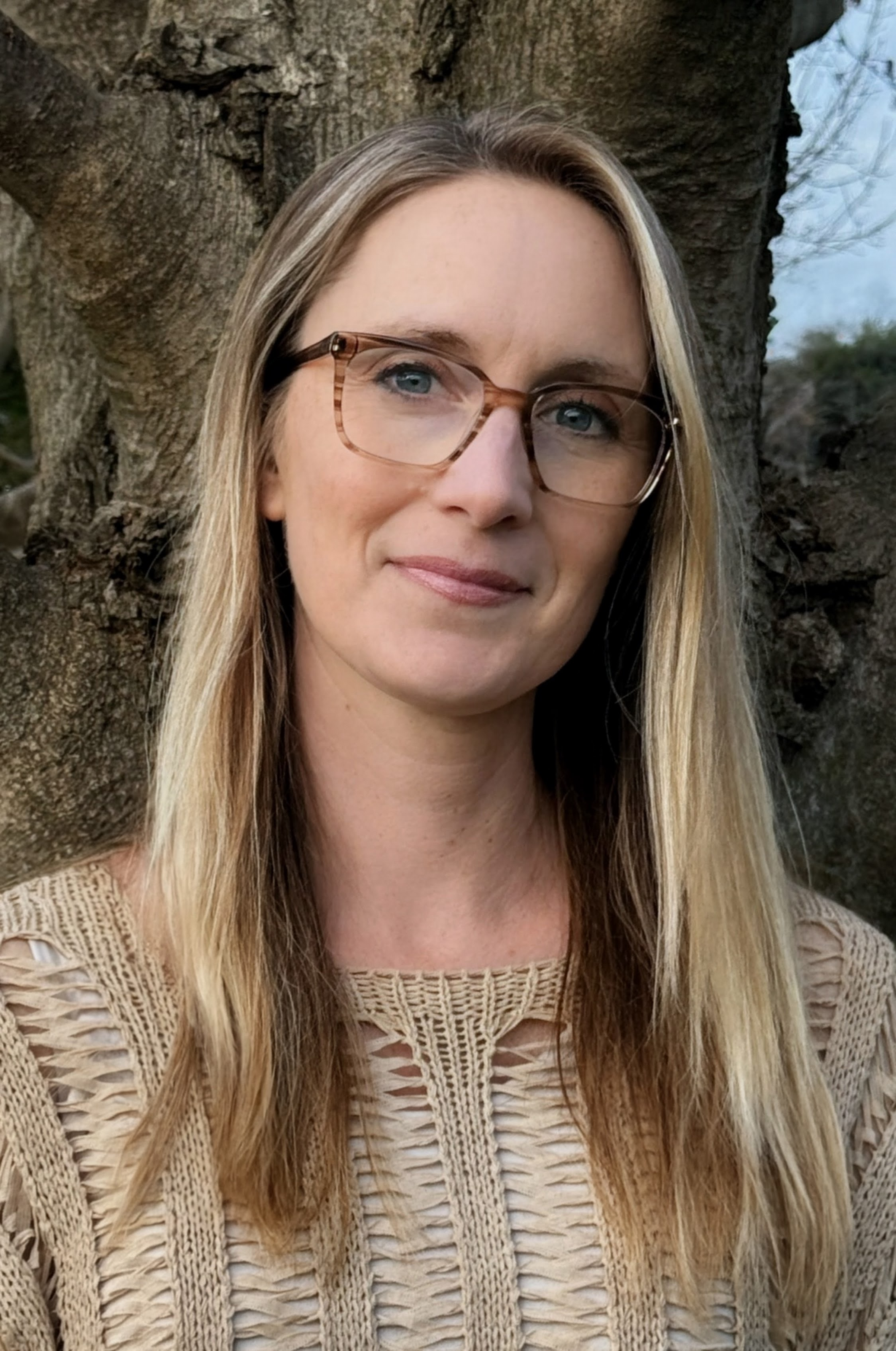A woman with blonde hair and glasses standing outdoors in front of a large rock formation.