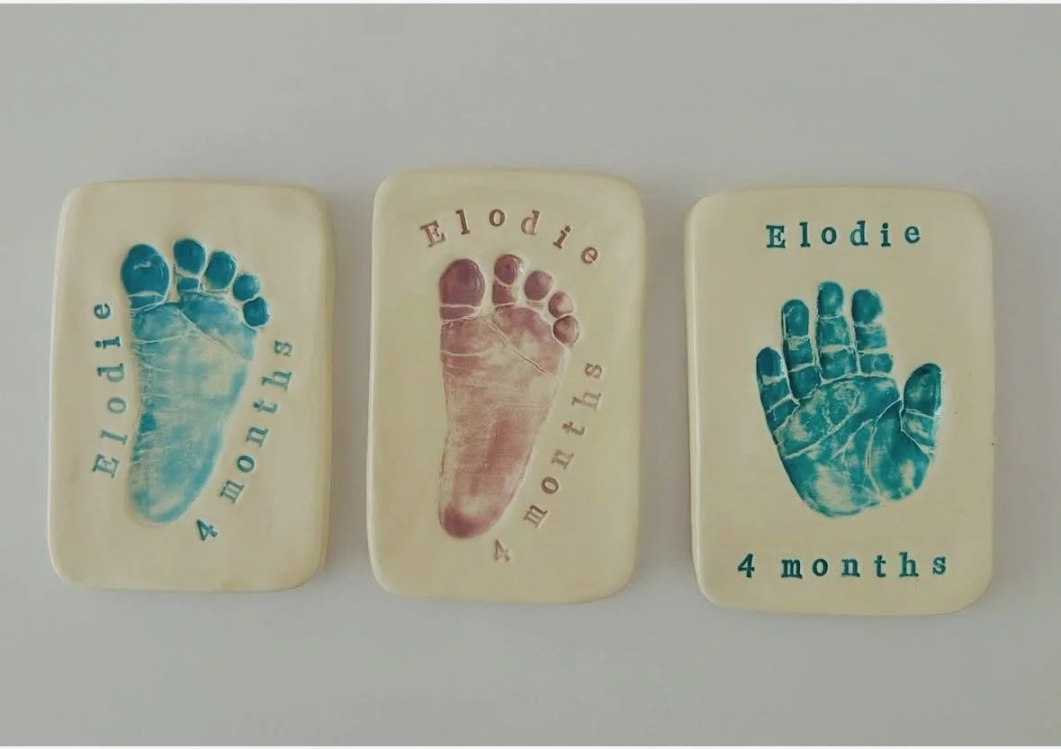 Three glazed paperweights with baby footprints and stamps. The first has a blue footprint with "Elodie 4 months," the second has a pink footprint with "Elodie 4 months" and the third has a blue footprint with "Elodie 4 months."