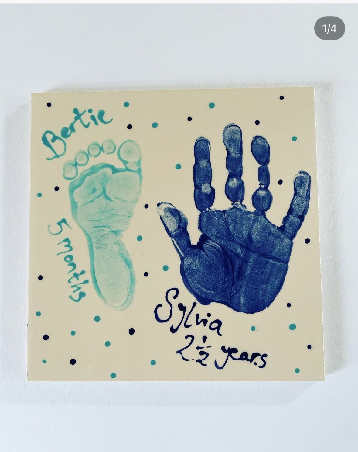 A large tile with two handprints, one smaller in green labelled 'Berit 5 months' and one larger in blue labelled 'Sofia 2 ½ years', surrounded by small blue and black dots.