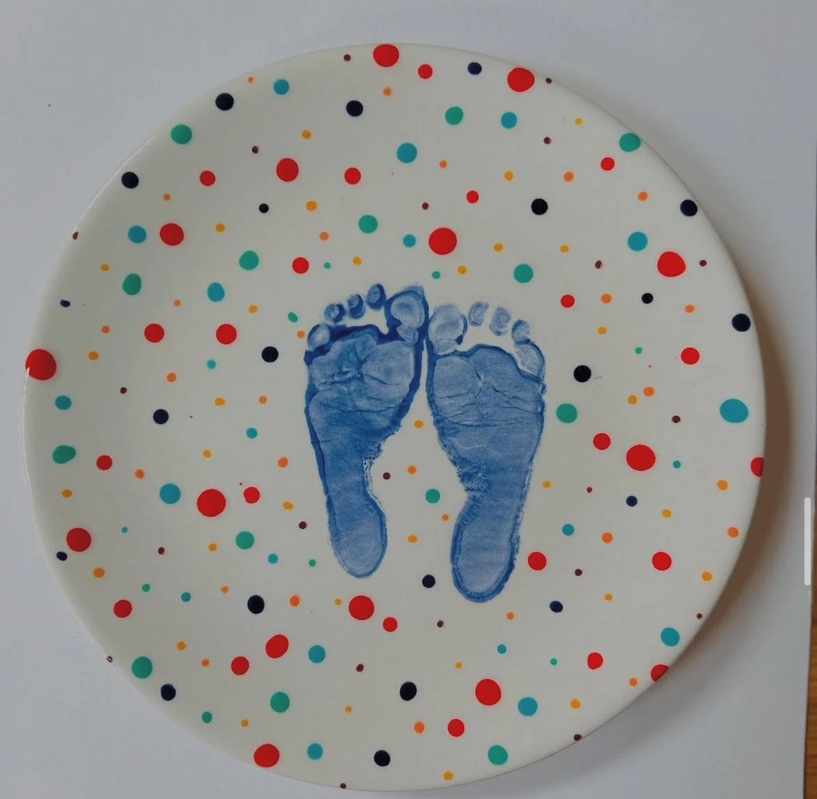 A round plate with colorful polka dots and a blue baby footprint in the center.