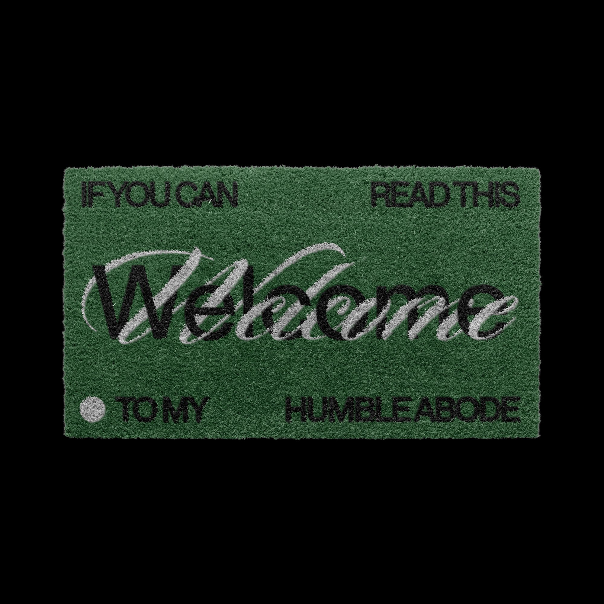 Green doormat with the word 'Welcome' and phrases 'If you can read this,' 'Tomy,' and 'Humble Abode' in black text.