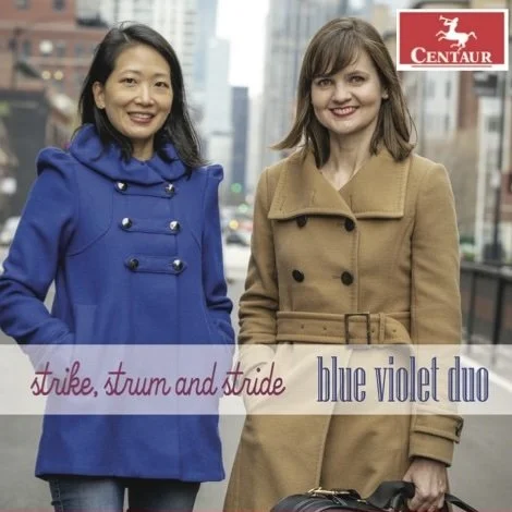 Two women standing outdoors in an urban setting, smiling at the camera. One is wearing a blue coat with decorative buttons, and the other is wearing a tan coat. There is a city skyline in the background. The image includes text referencing 'strike, strum and slide,' 'blue violet duo,' and the Centaur logo.