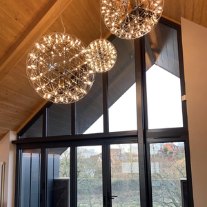Three spherical pendant lights hanging from a wooden ceiling in a room with large windows showing trees outside.
