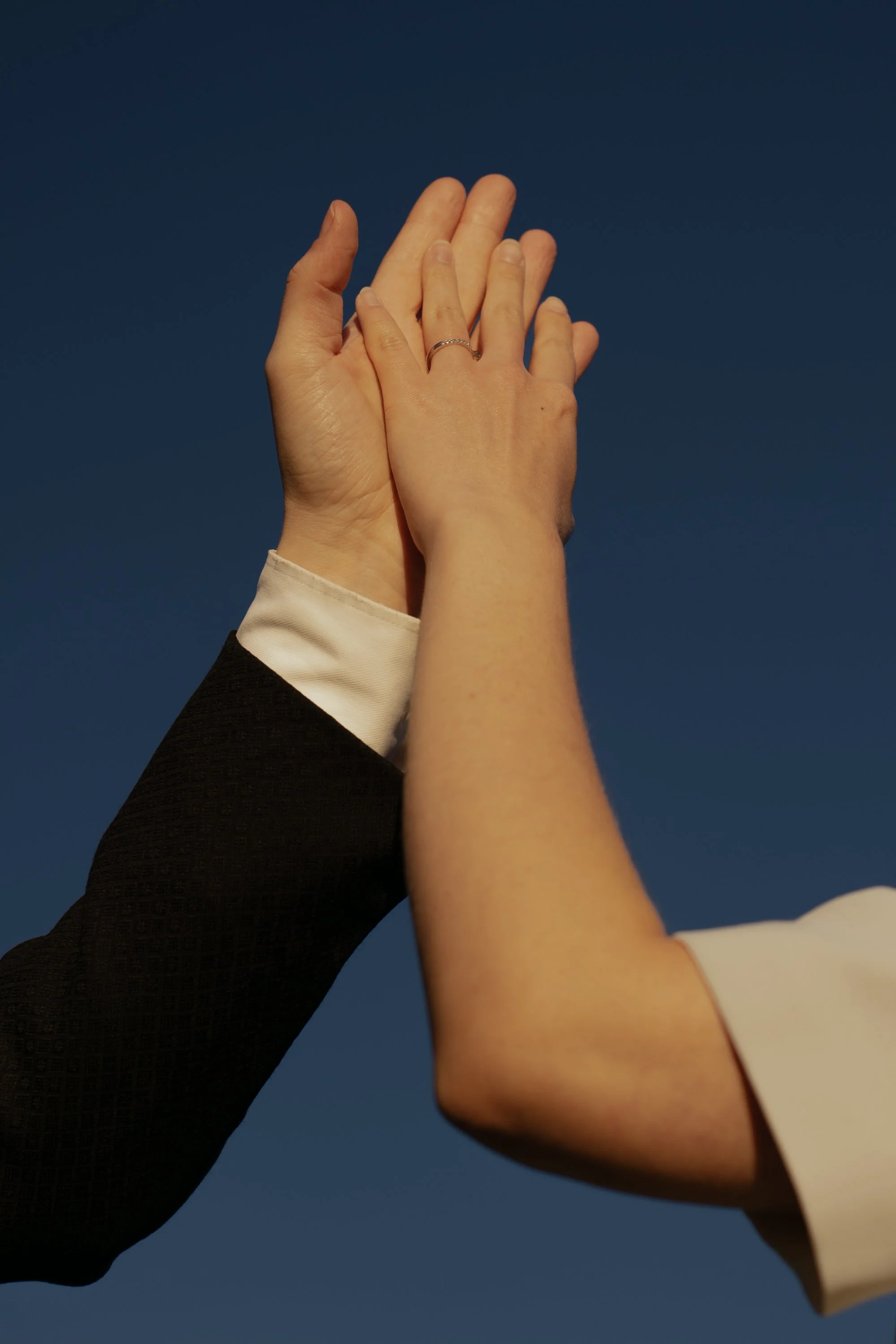 Two hands, one in a black sleeve and the other in a white sleeve, meeting hands against a dark blue background.