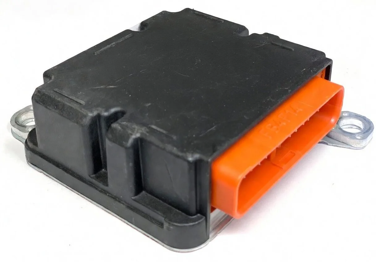 An automotive electronic control module with a black plastic housing and an orange connector, mounted on metal brackets.