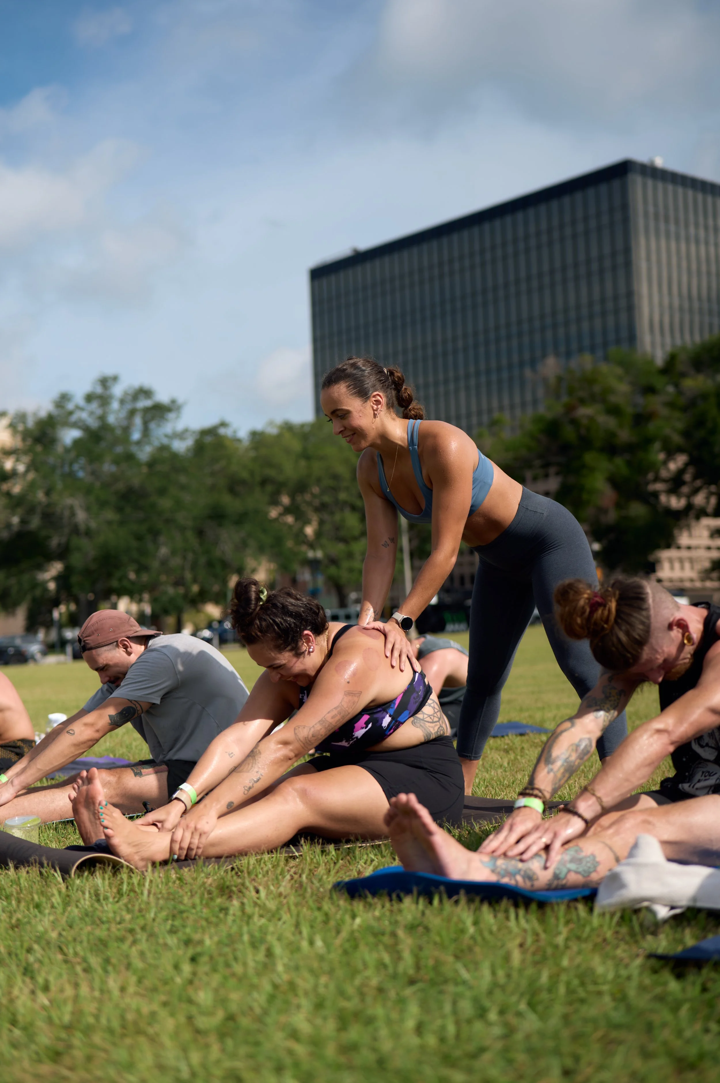 students in seated forward fold with yoga teacher providing one of them with a hands on assist