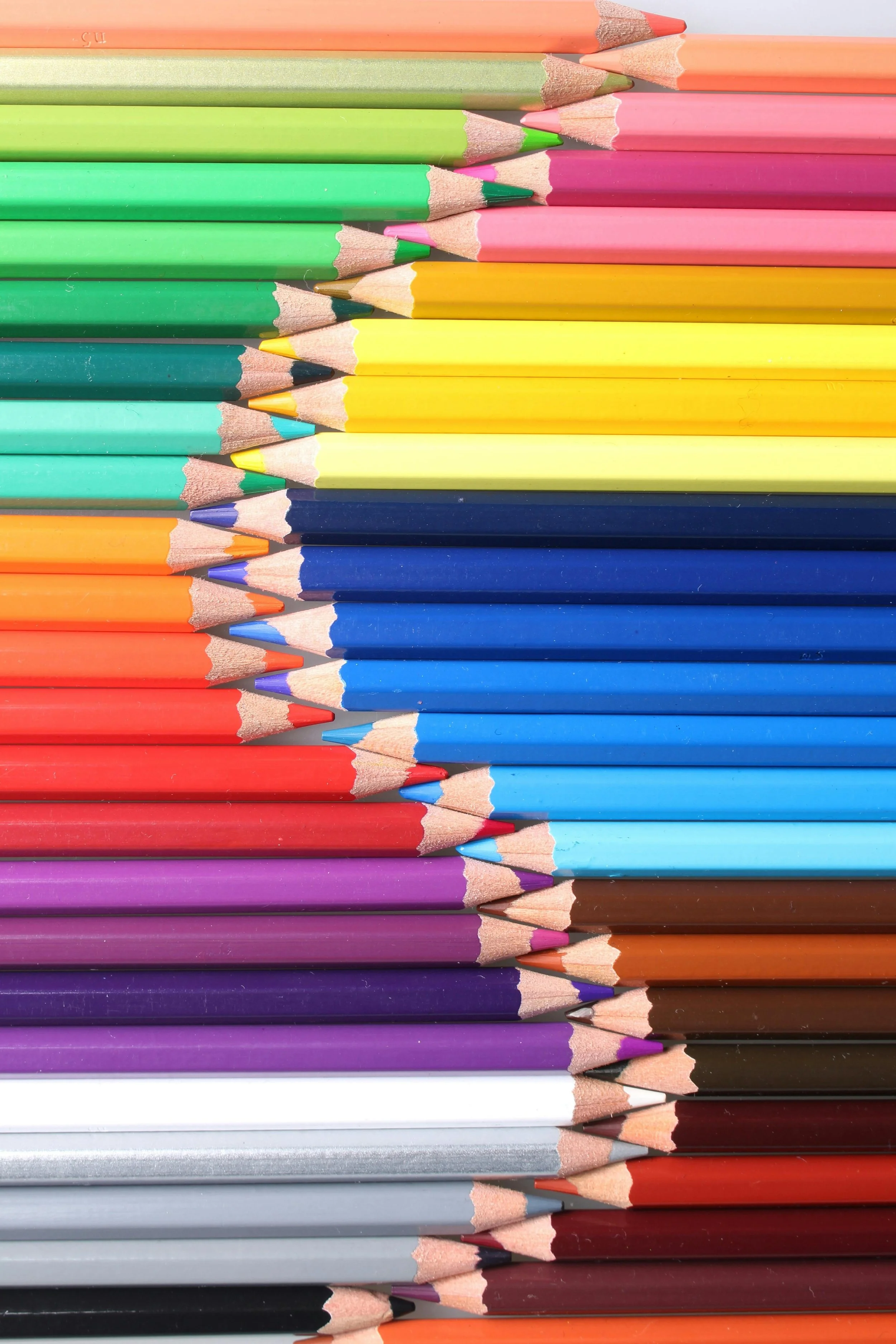 A close-up of neatly arranged colored pencils, showing sharpened tips in various colors including pastel shades, bright colors, and dark hues, stacked horizontally.