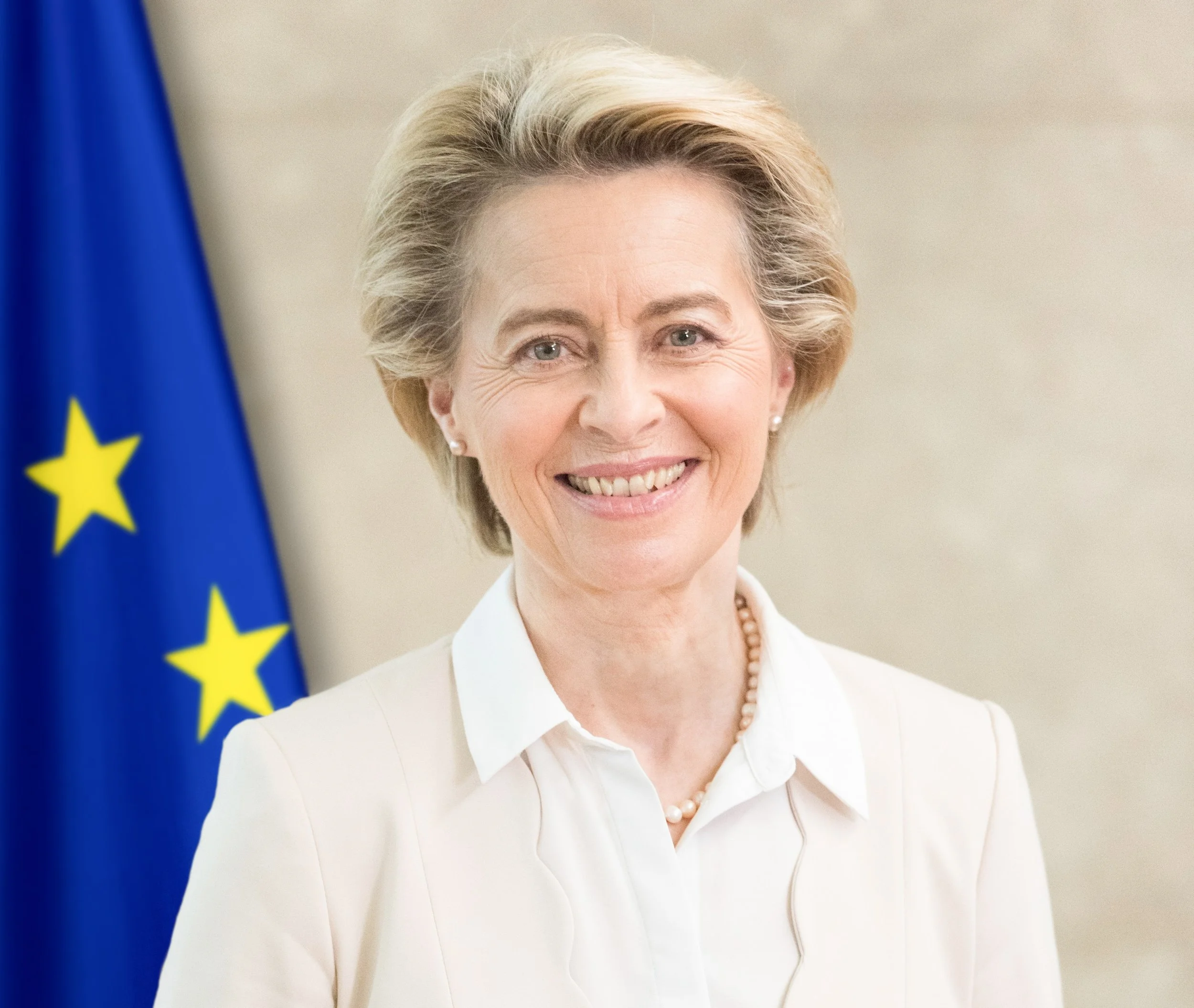 A woman with short blonde hair smiling in front of a European Union flag.
