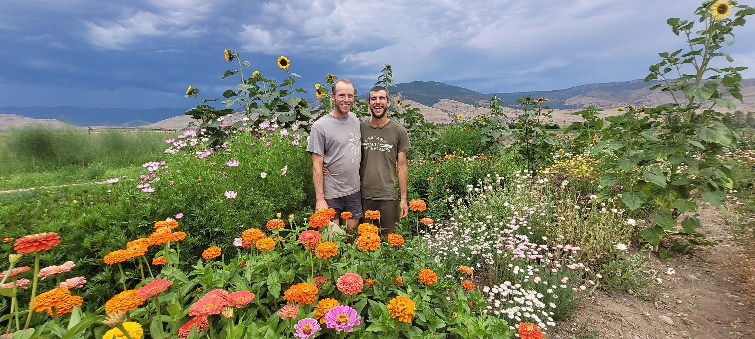 Josh and Adam of Forkbound Farm smiling in a field of flowers with mountains in the background.