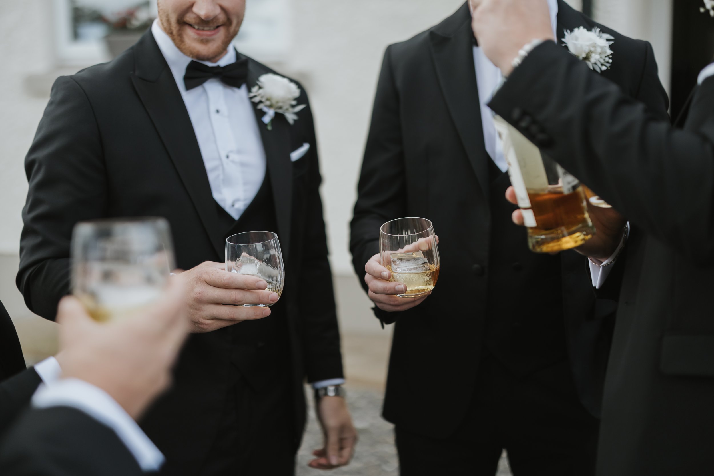 Group of men in black tuxedos celebrating with drinks at a formal event.