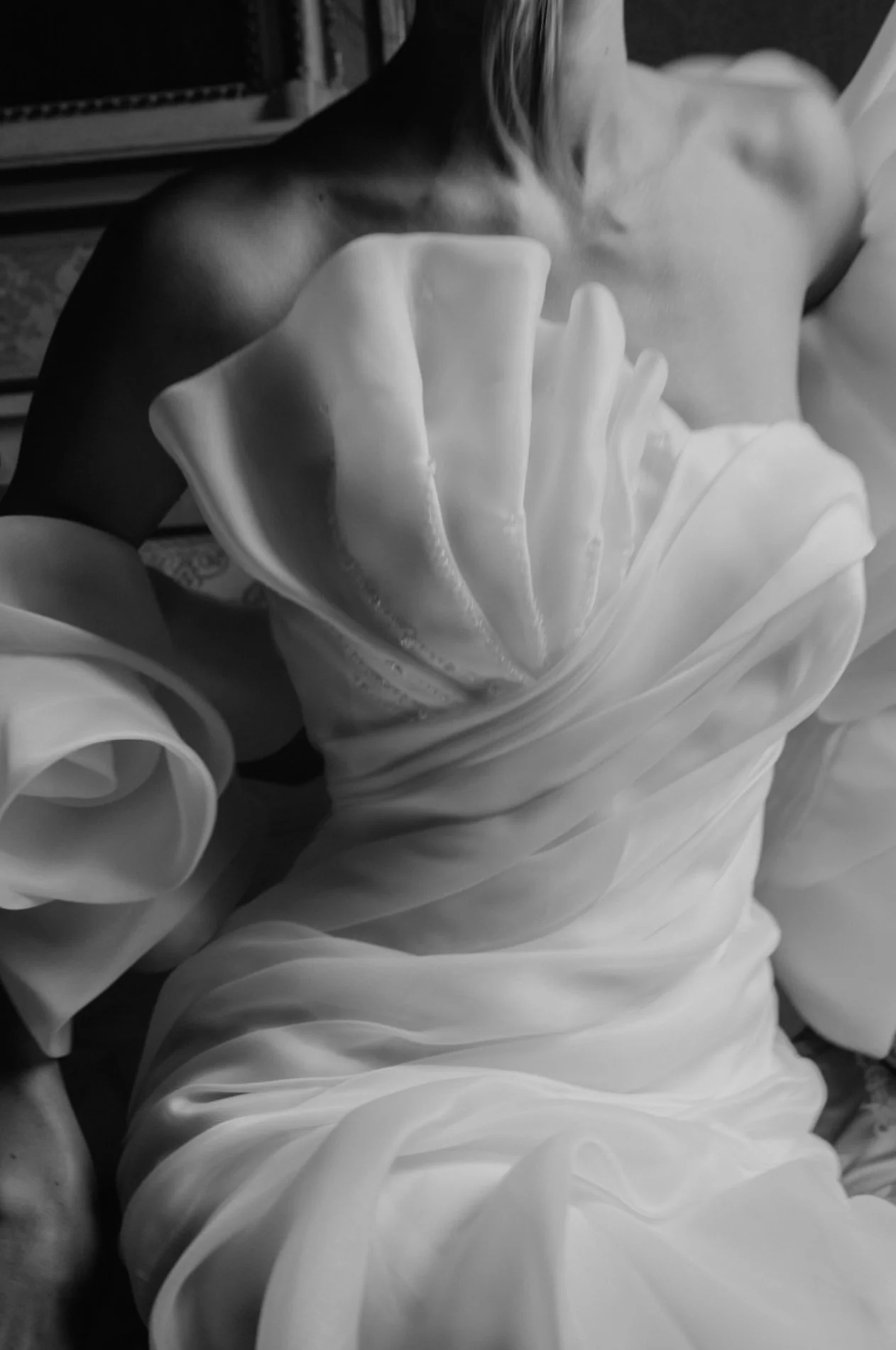 A woman in a strapless dress is sitting, with the focus on her upper body and part of her dress, in black and white.