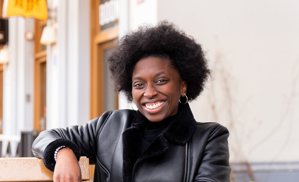 Vrouw met afrohaar die glimlacht en op een bank zit indoors.