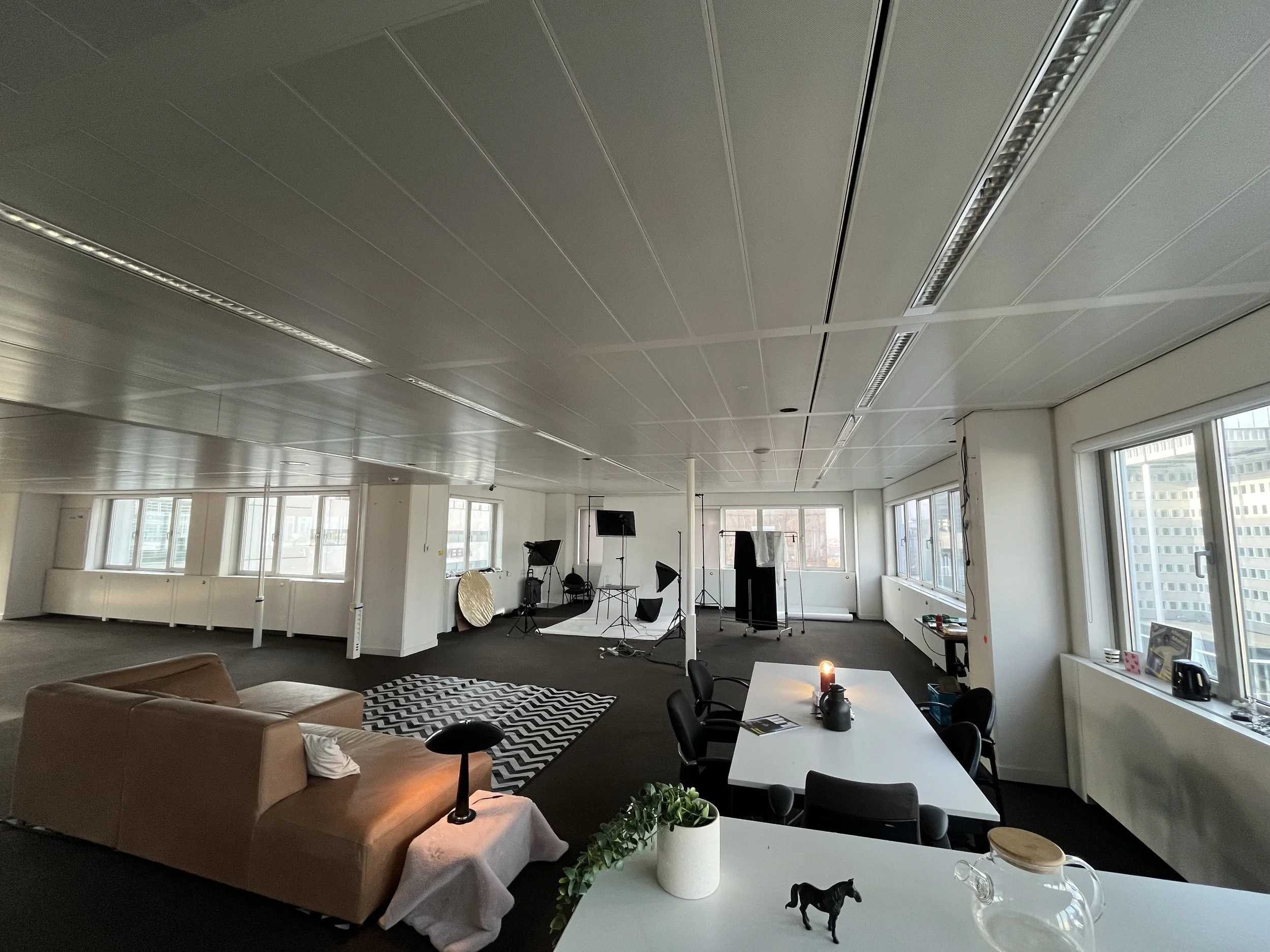 Studio Mickpunt in Rotterdam. Interior of an office or studio with photography equipment, a seating area with a brown couch, and large windows letting in natural light.