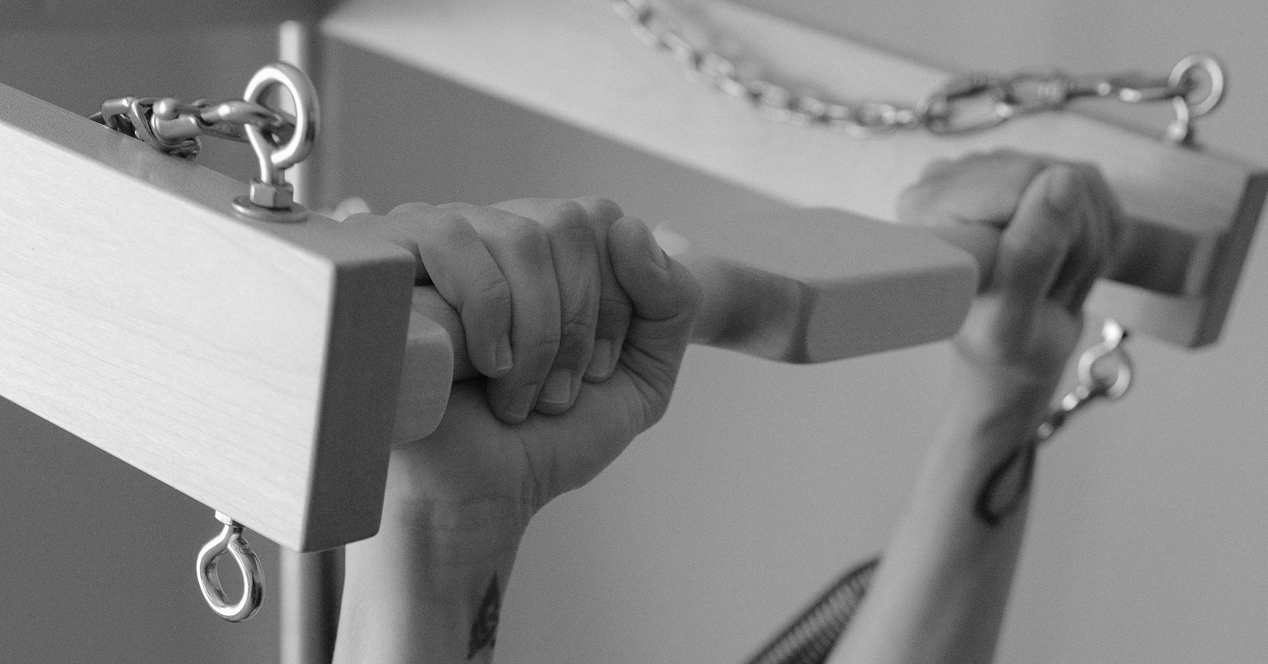 A person holding a wooden handrail with a metal chain attached to the side of a piece of furniture or equipment.