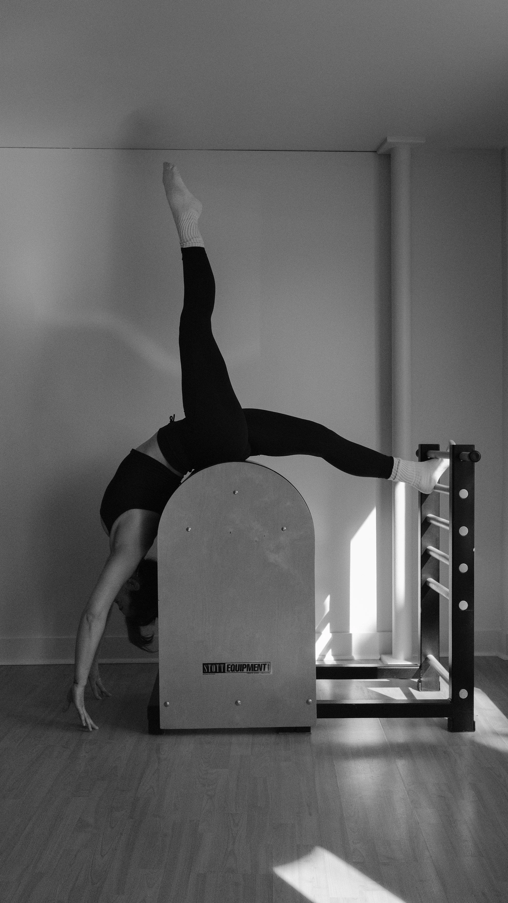 A person performing a handstand with their legs extended against a wall, using a piece of gym equipment in a room with wooden flooring.