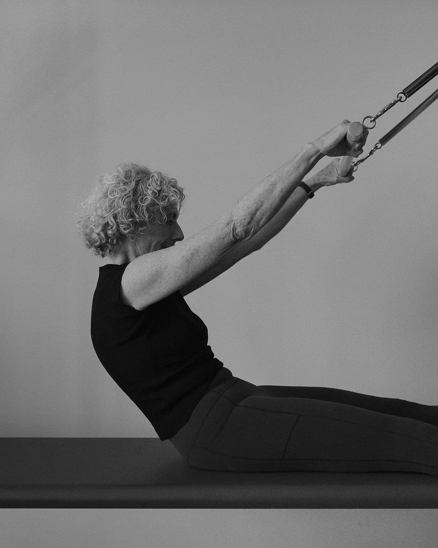 An elderly woman with curly hair doing an exercise with resistance bands while lying on a mat.