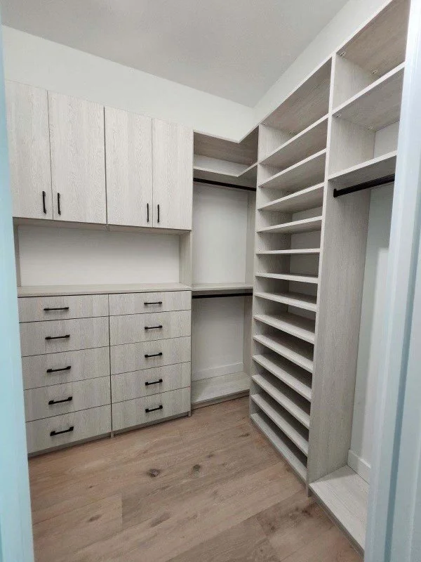 Empty walk-in closet with built-in cabinets, drawers, and open shelving in a modern design.