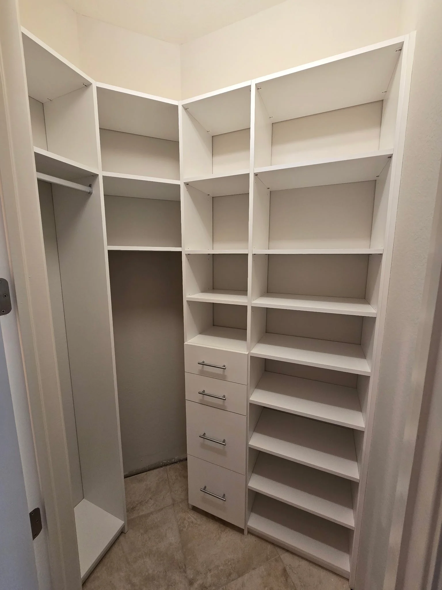 Empty white walk-in closet with multiple shelves, drawers, and hanging rods.
