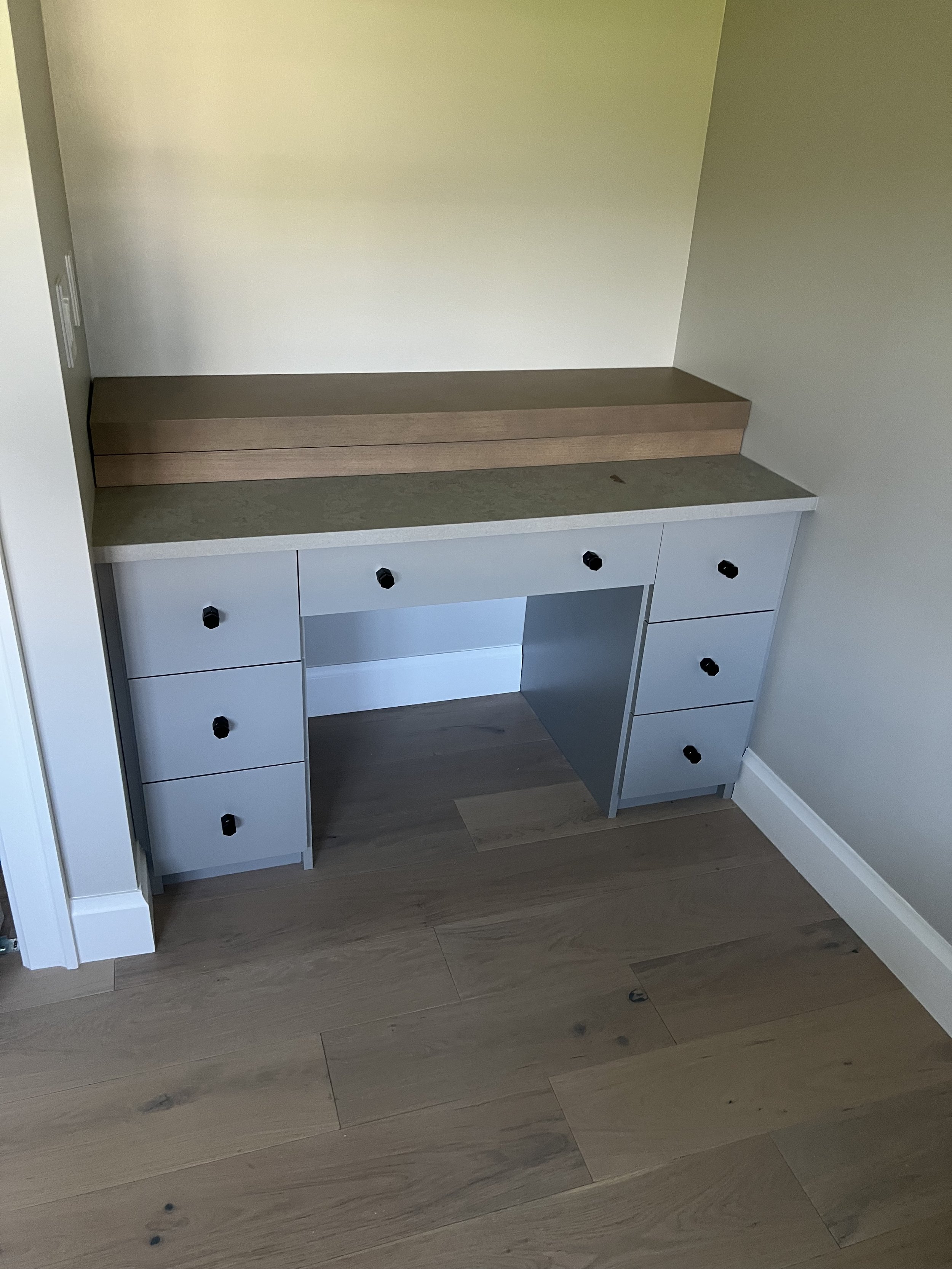 Empty built-in desk with drawers, a marble countertop, and an open space for a chair, situated in a room with light-colored walls and wooden flooring.