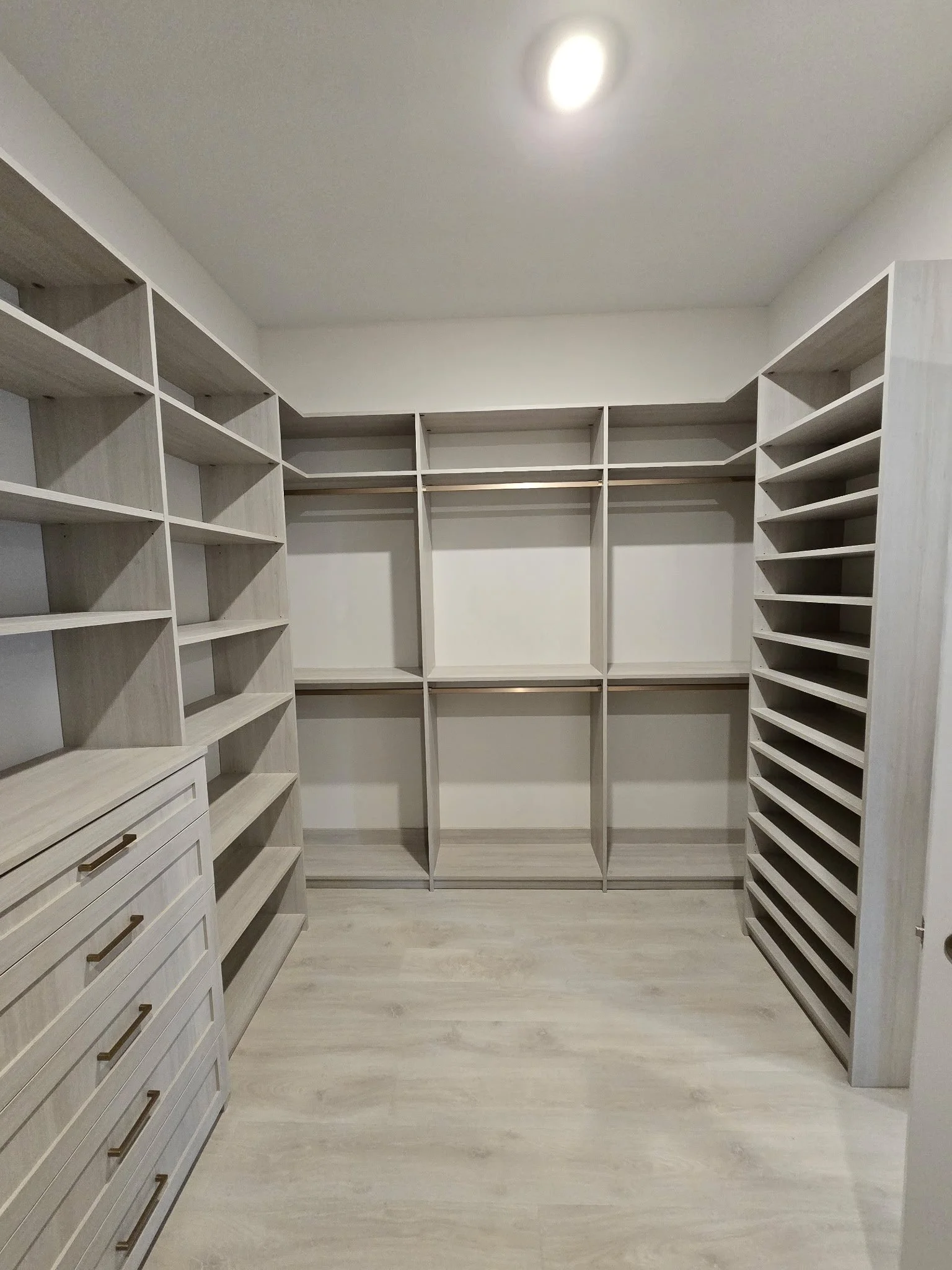 Empty walk-in closet with built-in wooden shelves, drawers, and a hanging rod.