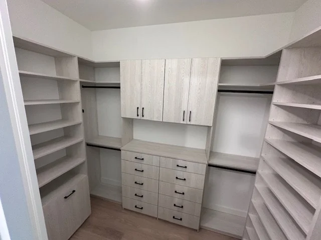 Empty walk-in closet with white built-in shelves, drawers, and hanging spaces.