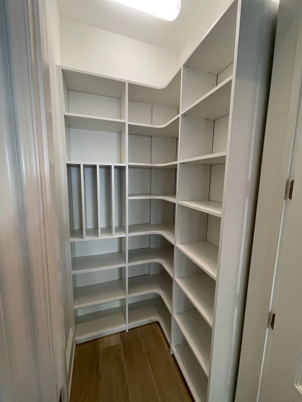 Empty white built-in corner shelving unit with multiple shelves near a doorway, with wood flooring underneath.