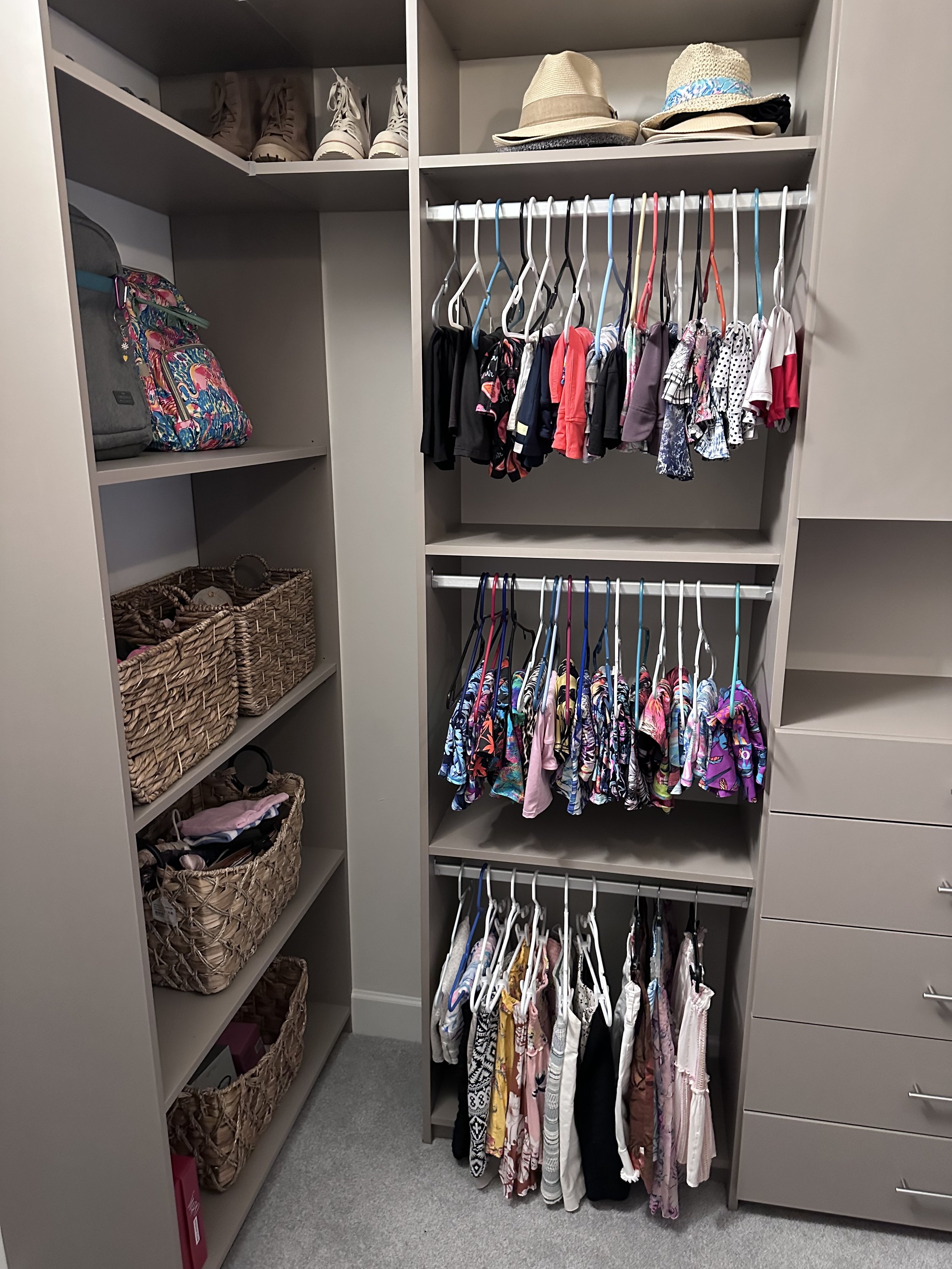 A closet with organized shelves and clothes on hangers, including hats on the top shelf and baskets on the side shelves.