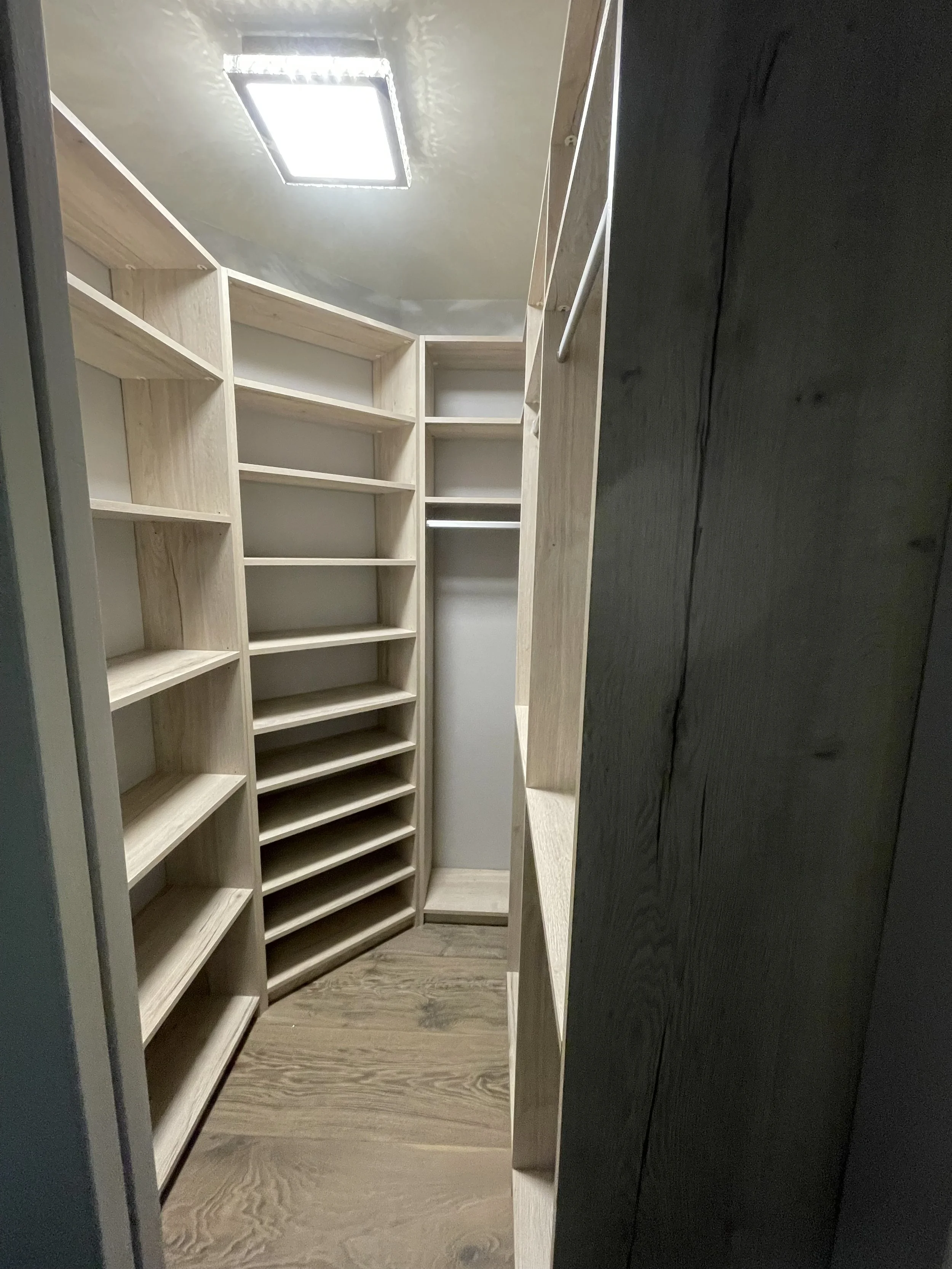 Empty walk-in closet with built-in wooden shelves and a wooden floor, illuminated by a ceiling light.