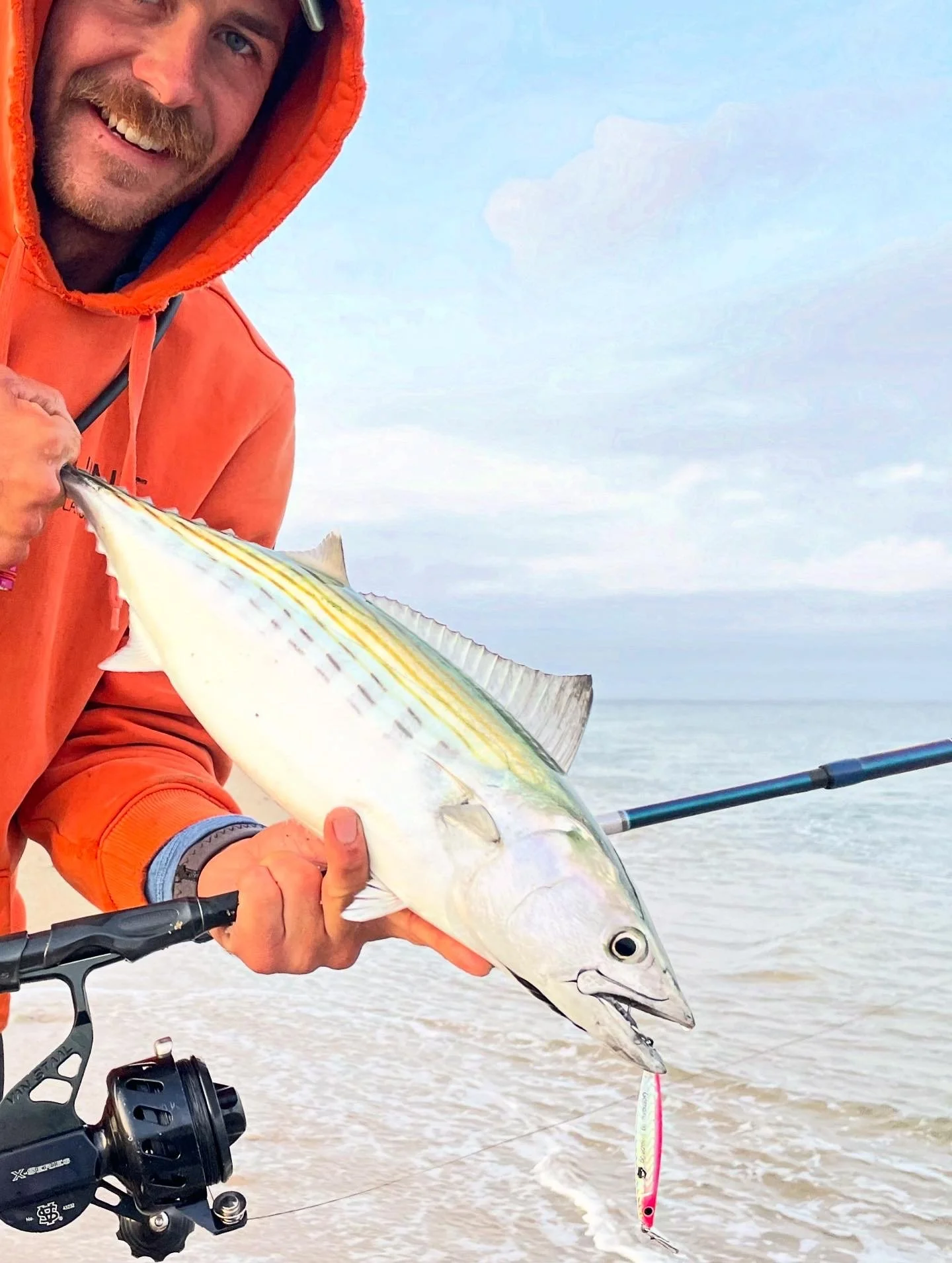 One of our expert guides holding a large Bonito caught while fishing on a beach, with the ocean and sky in the background.