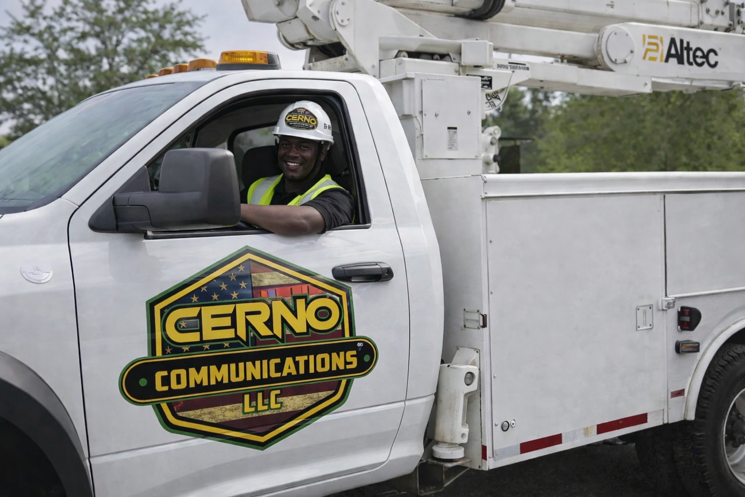 A smiling man in a safety vest and helmet sitting in the driver's seat of a utility truck with a large utility bucket attached to the back. The truck's door features a logo for Cerno Communications LLC.