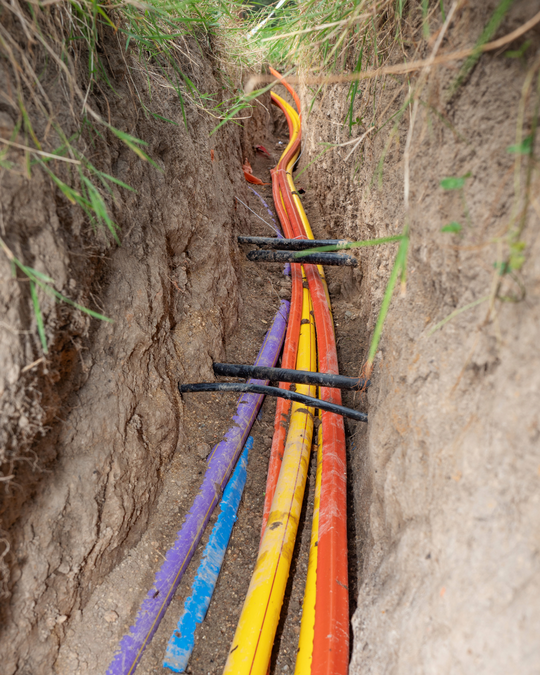 Color-coded pipes in a narrow trench for underground utility installation.