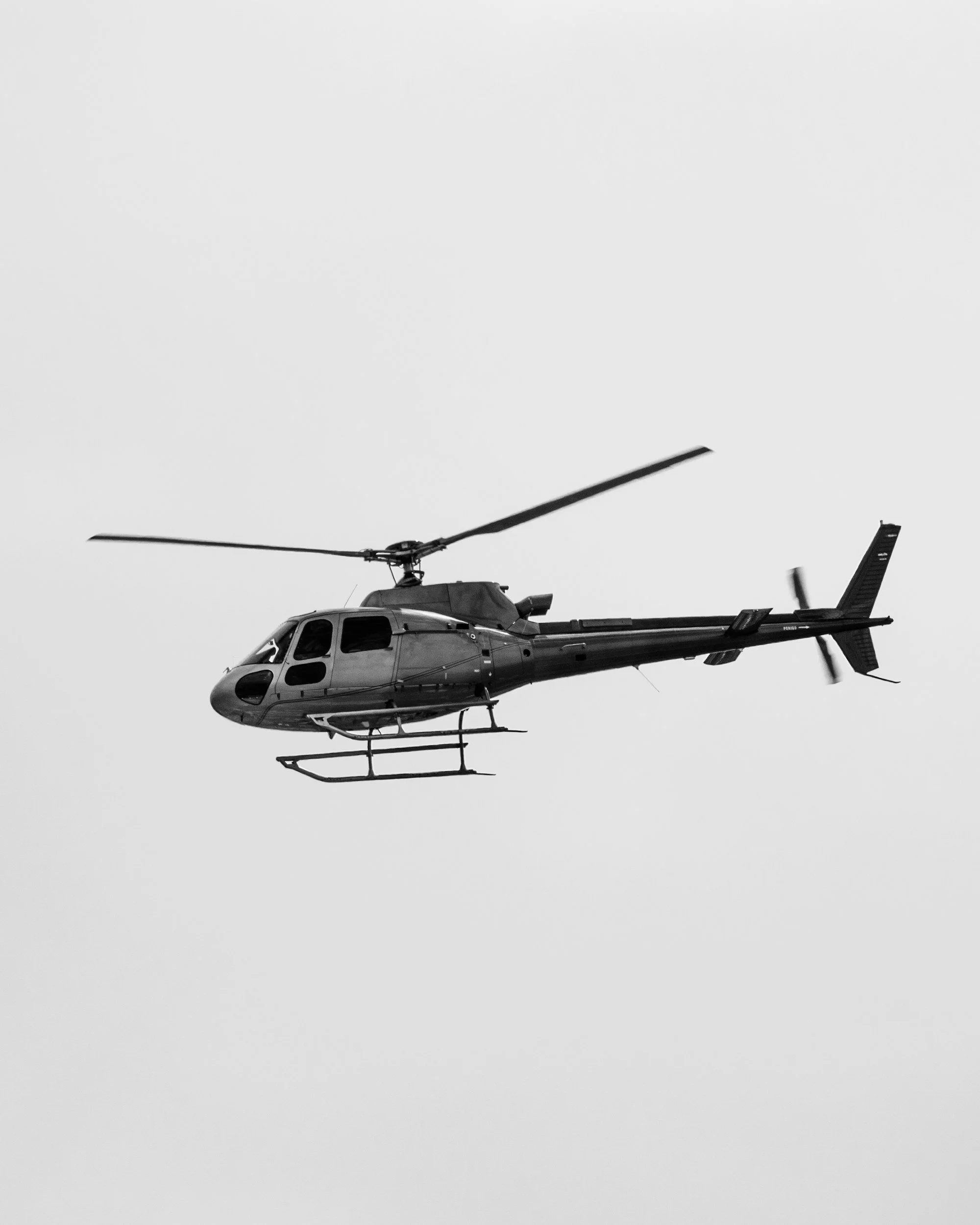 A black and white photo of a helicopter flying in the sky.