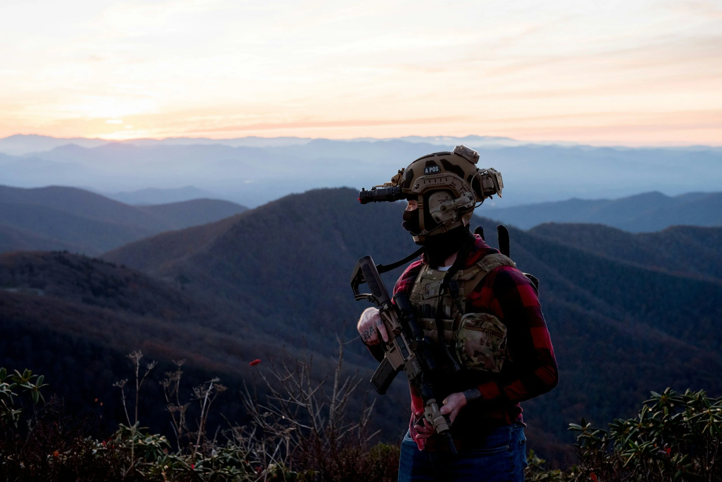 Soldier wearing a helmet and tactical gear overlooking mountainous landscape at sunset