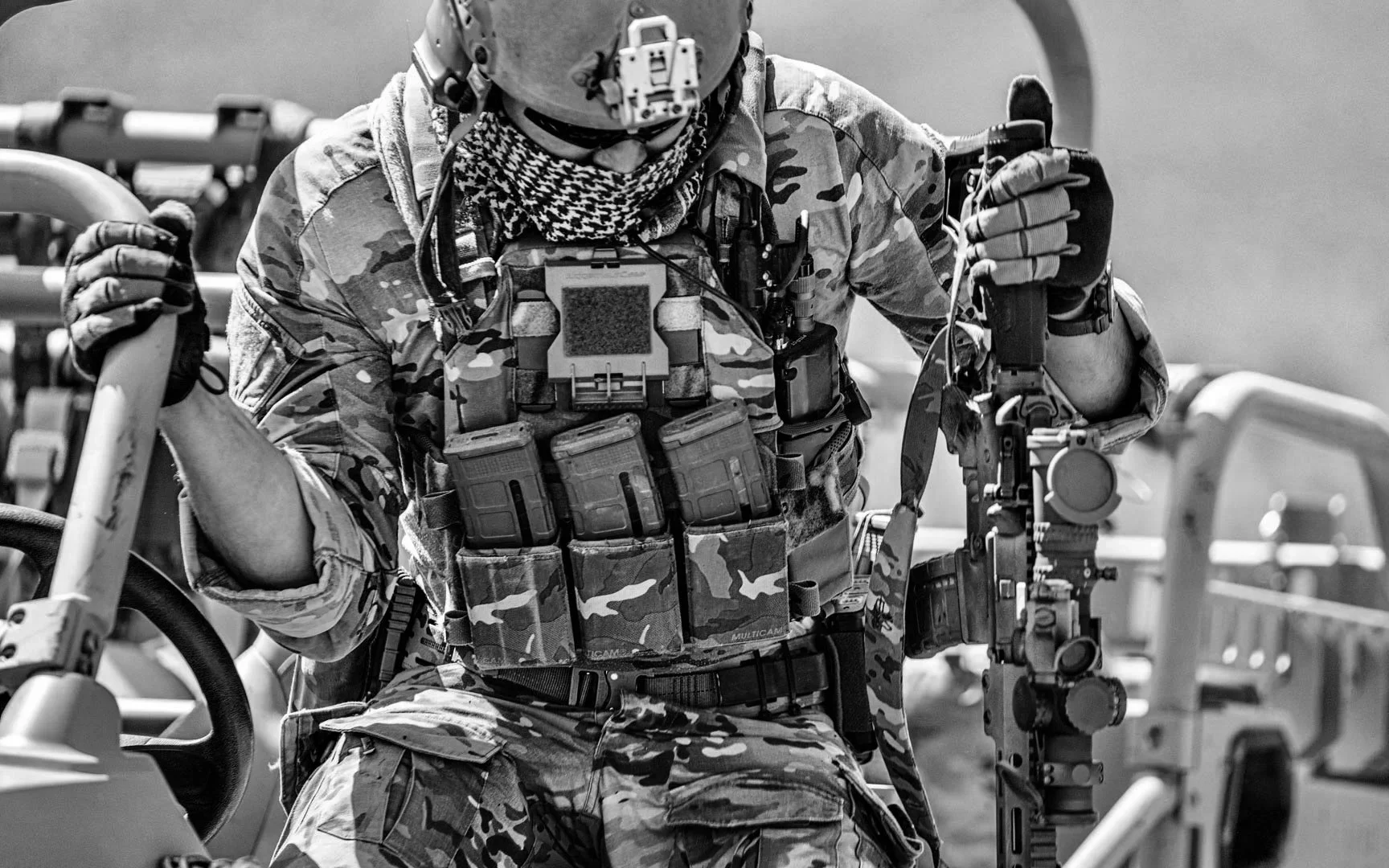 A soldier in camouflage uniform adjusting equipment on a military vehicle.