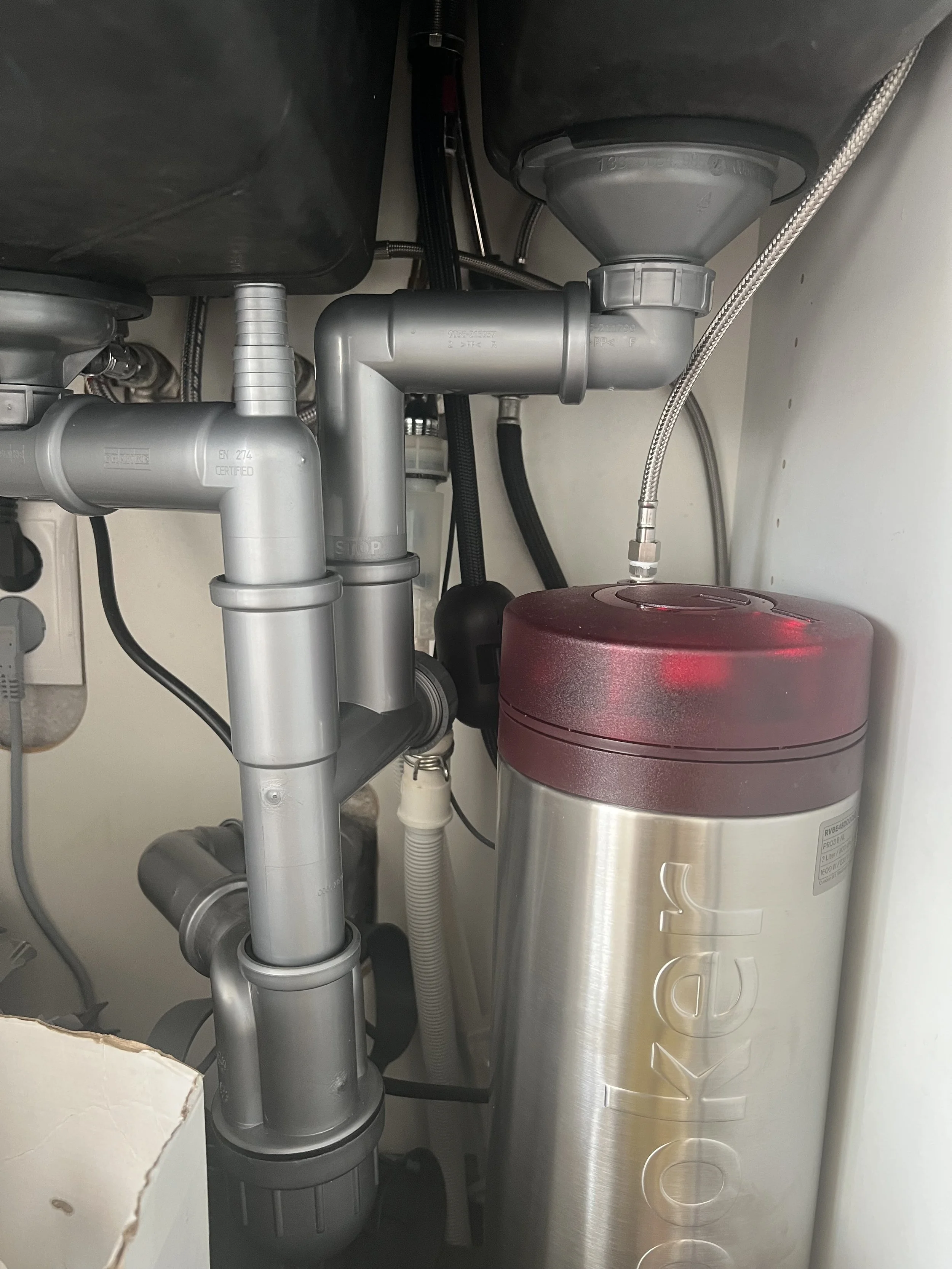 Under-sink plumbing with PVC pipes and a large vessel water filter system.