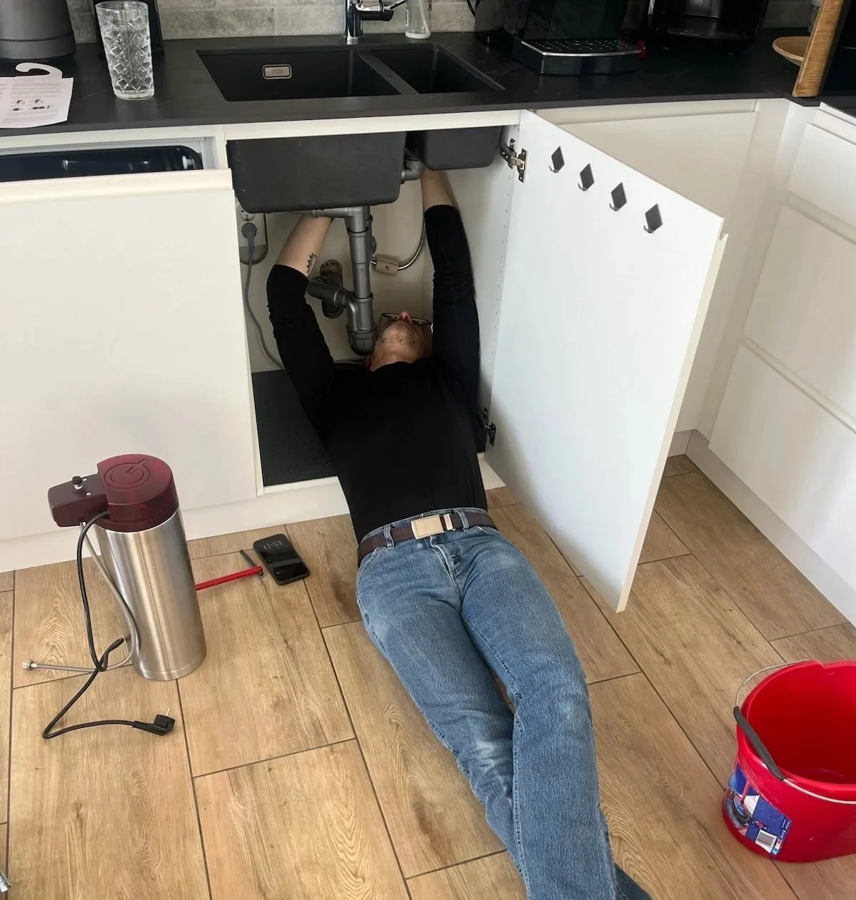 A man repairing a sink pipe under a kitchen sink.