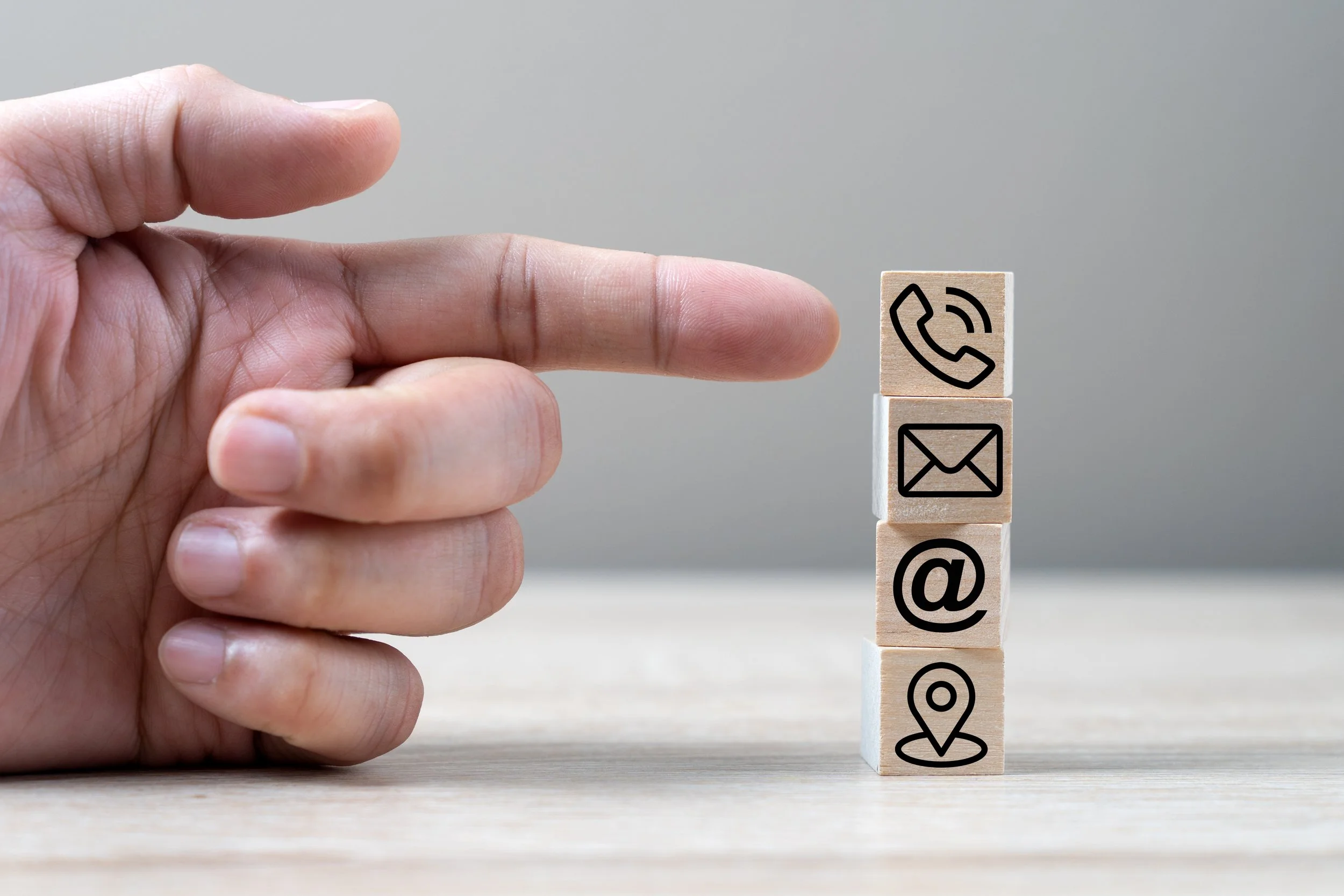 A hand with the index finger extended pointing at stacked wooden blocks with communication and location icons.