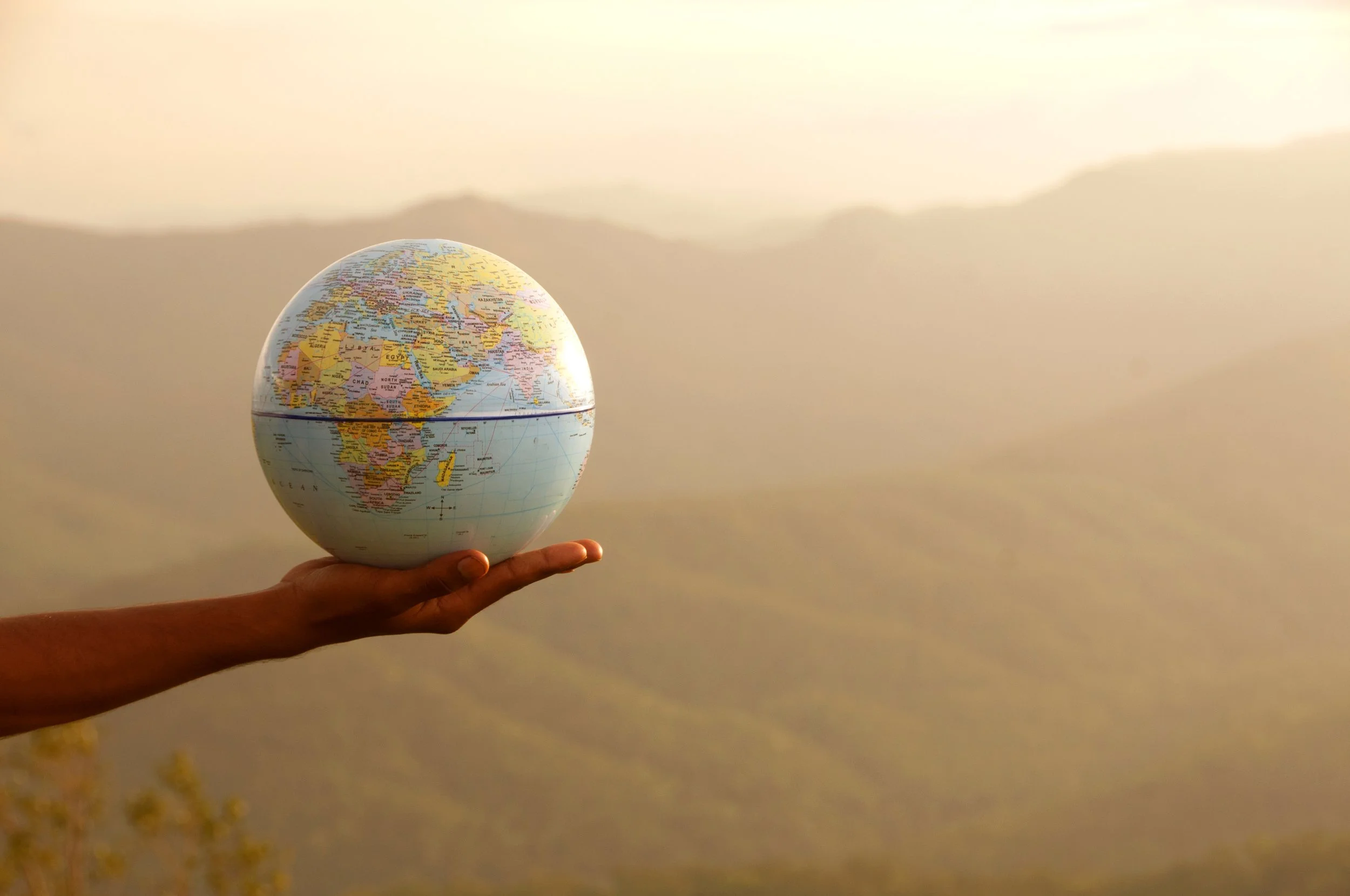 Person holding a globe shaped like a world map against a sunset sky.